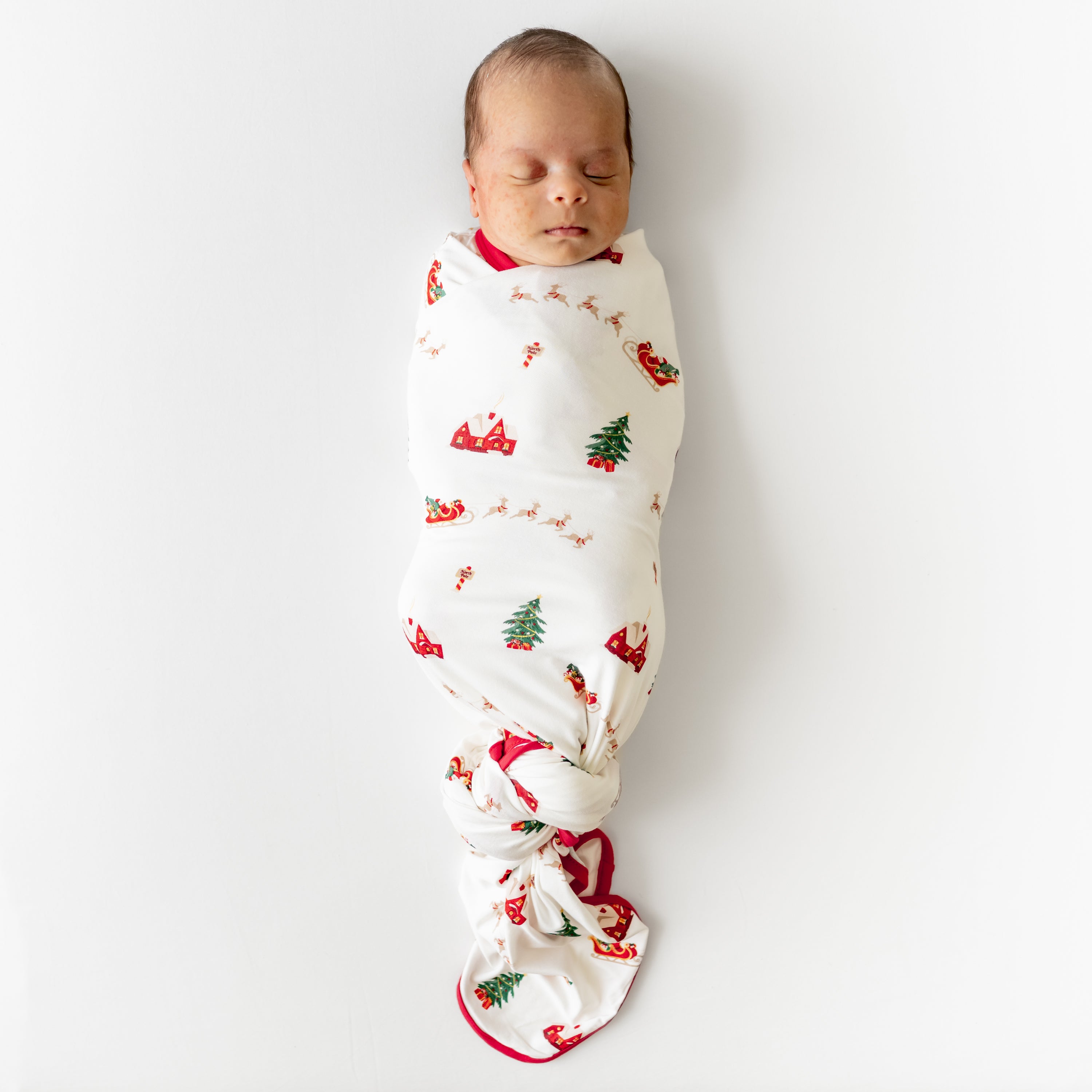 Sleeping newborn swaddled in the Swaddle Blanket in Santa Sleigh with a knotted bottom