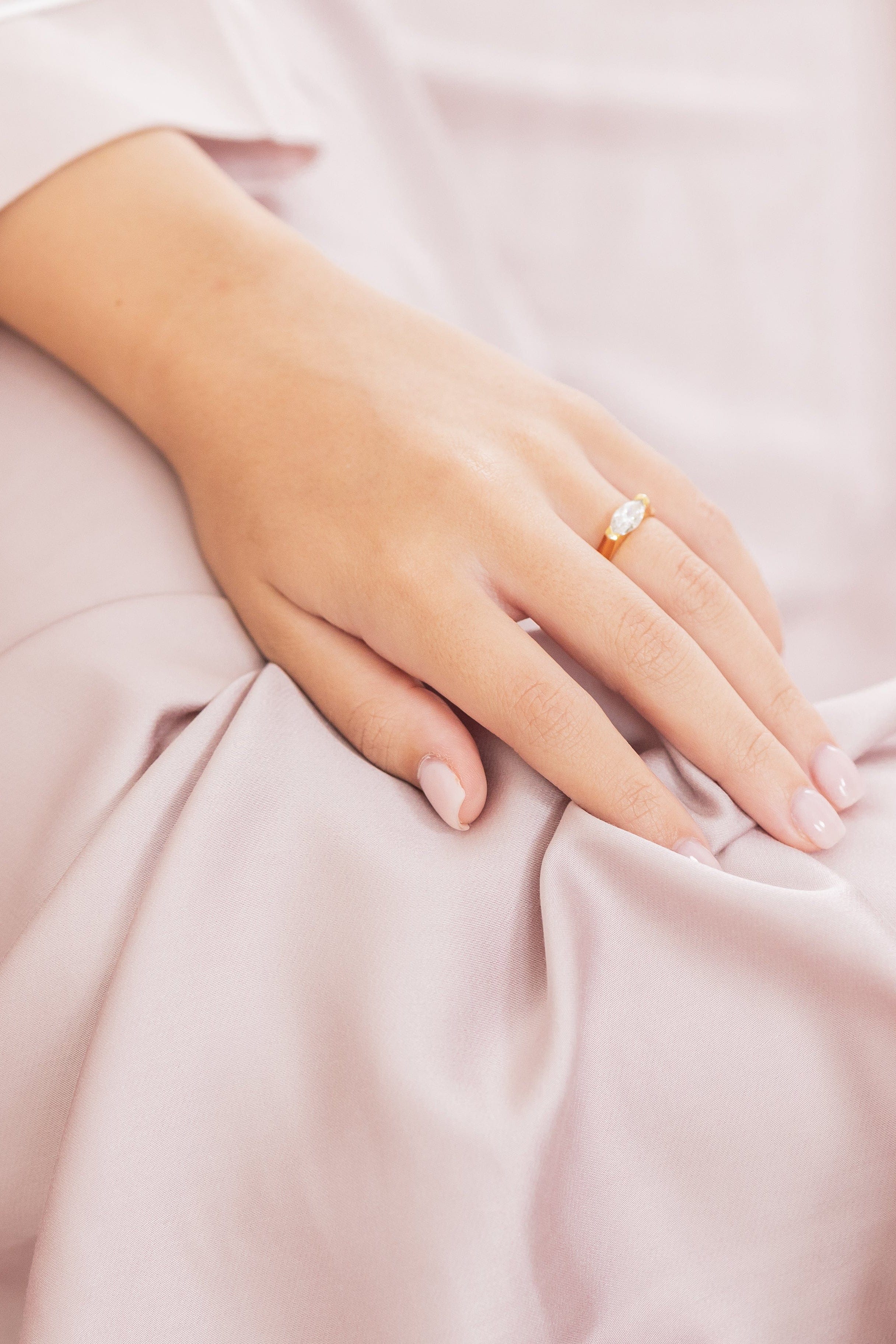 Hand with a ring on a soft pink fabric background
