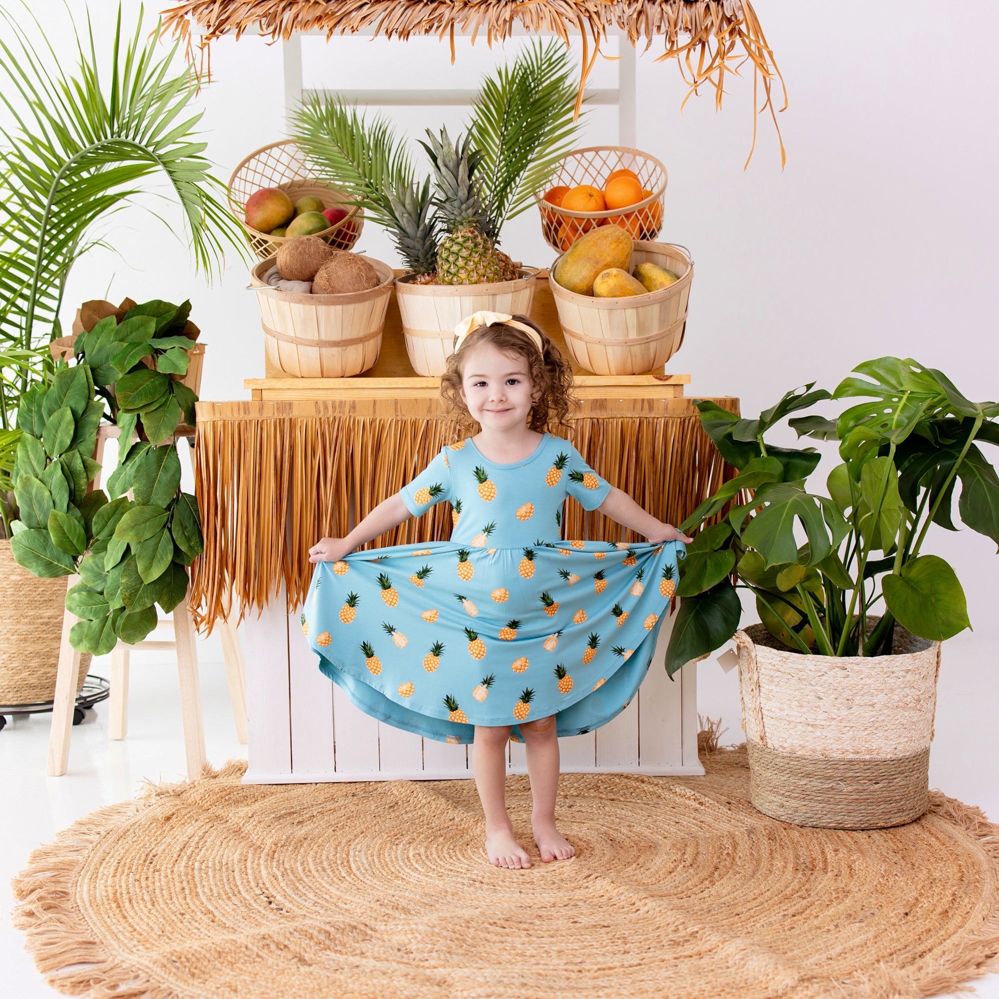 Toddler modeling Twirl Dress in Pineapple in front of fruit stand
