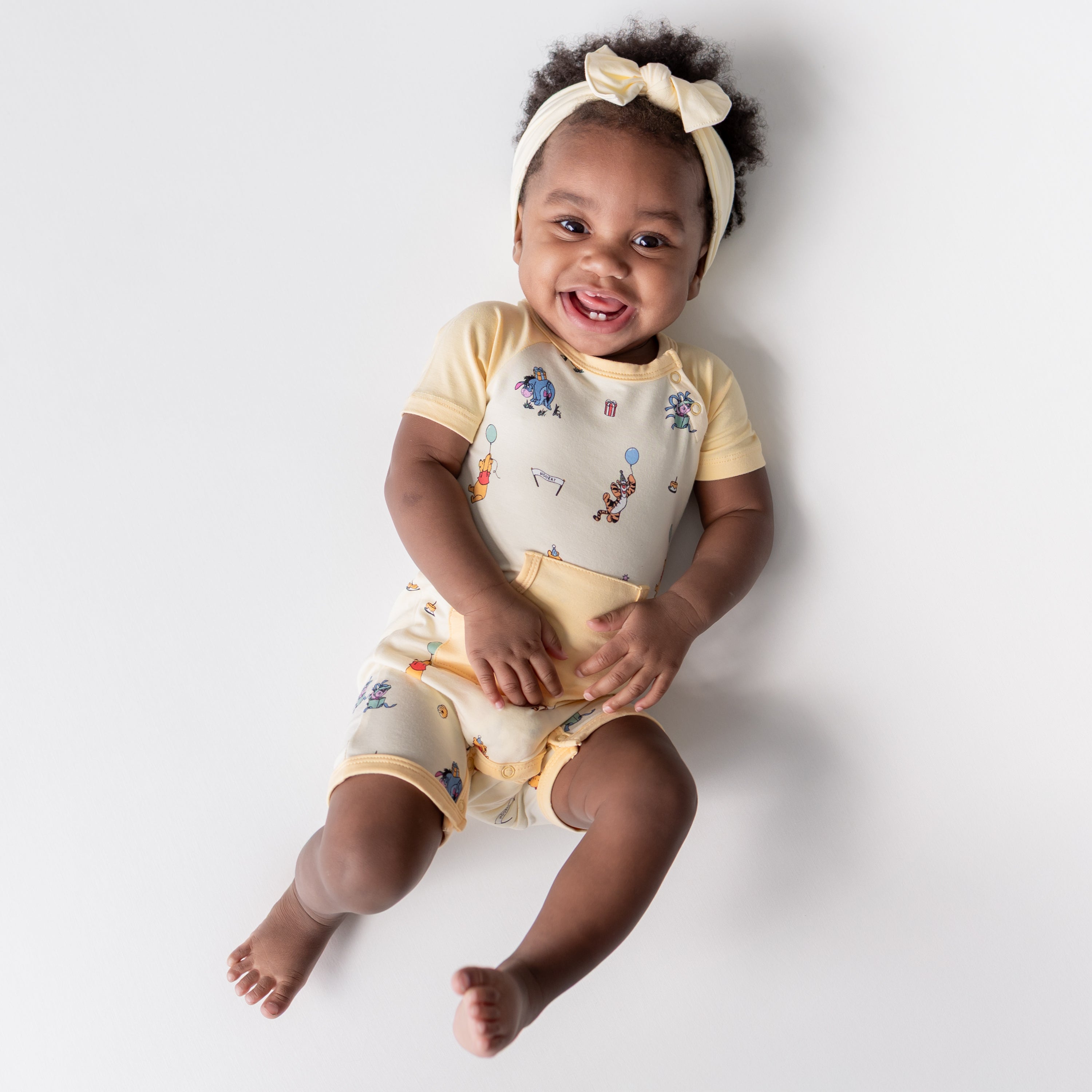Young toddler wearing the Shortall in Winnie the Pooh Celebration with a light yellow bow