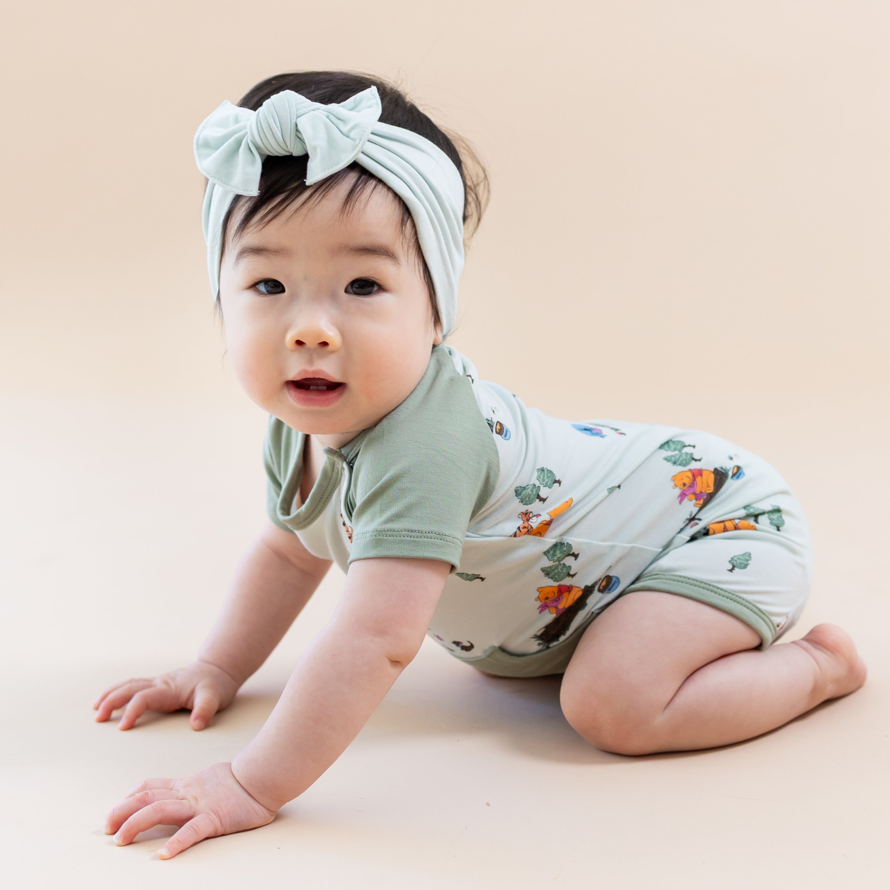 Young toddler crawling wearing the Shortall in Winnie the Pooh Hundred Acre Wood with light green bow