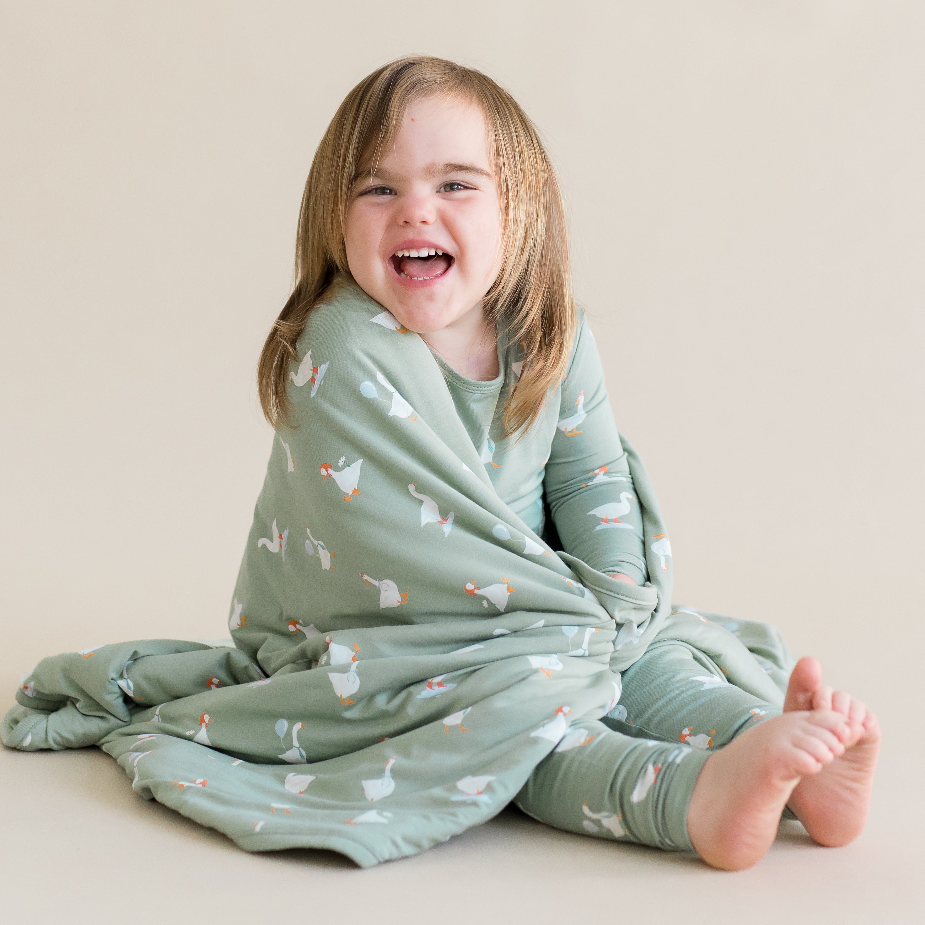 Child wrapped in a green patterned blanket with goose pattern on a beige background