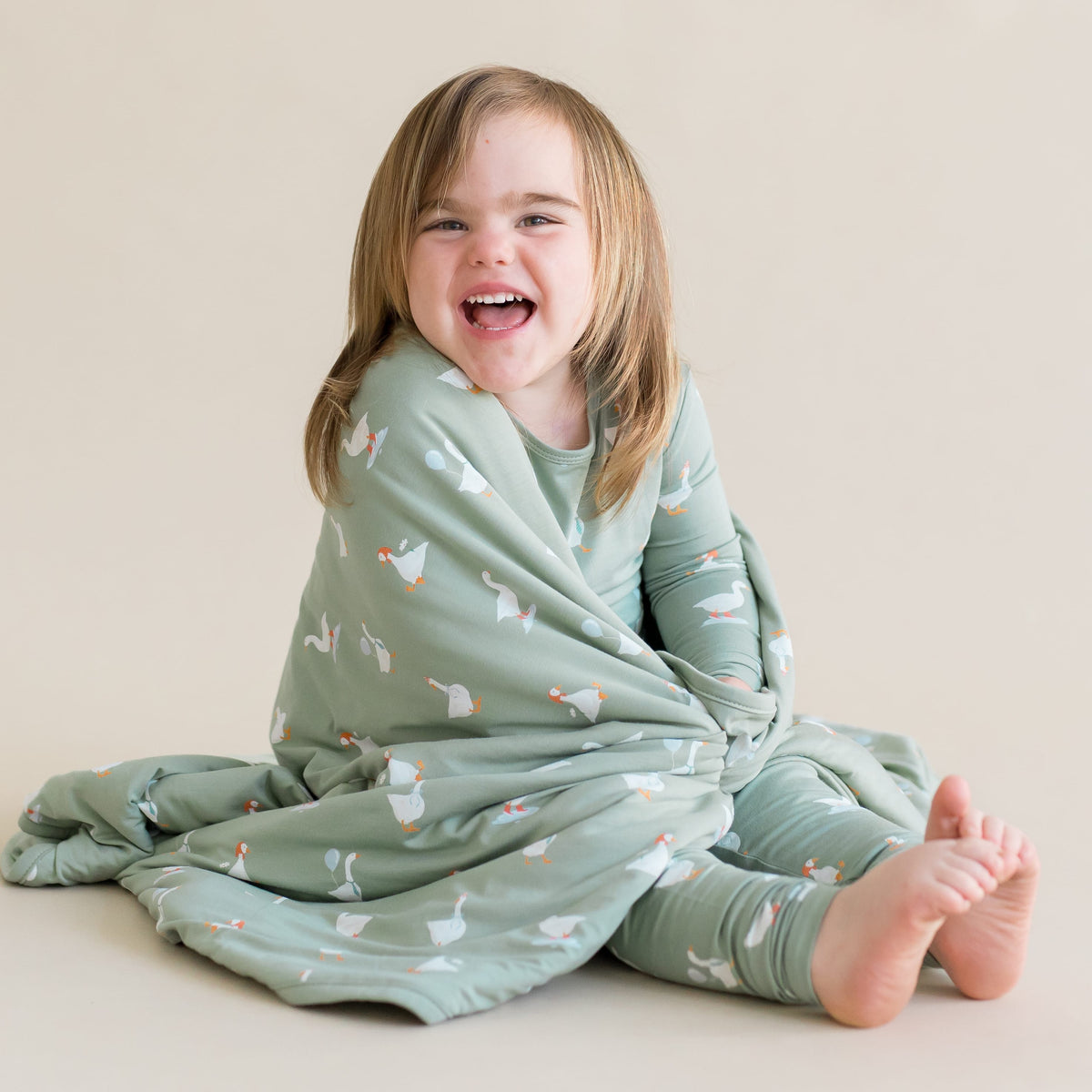 Child wrapped in a green patterned blanket with goose pattern on a beige background
