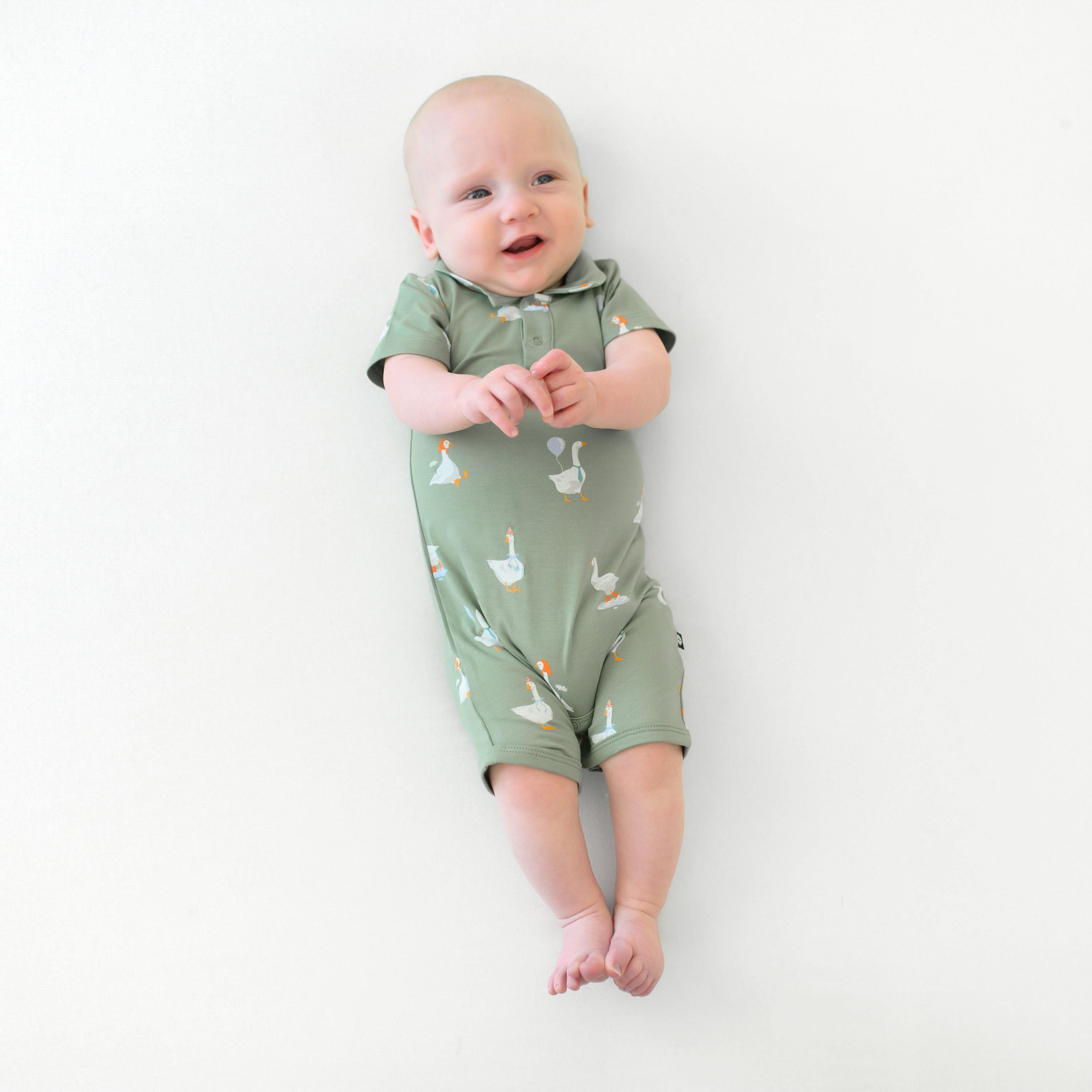 Infant laying down with his hands clasped in front of him wearing the Polo Shortall in Silly Goose