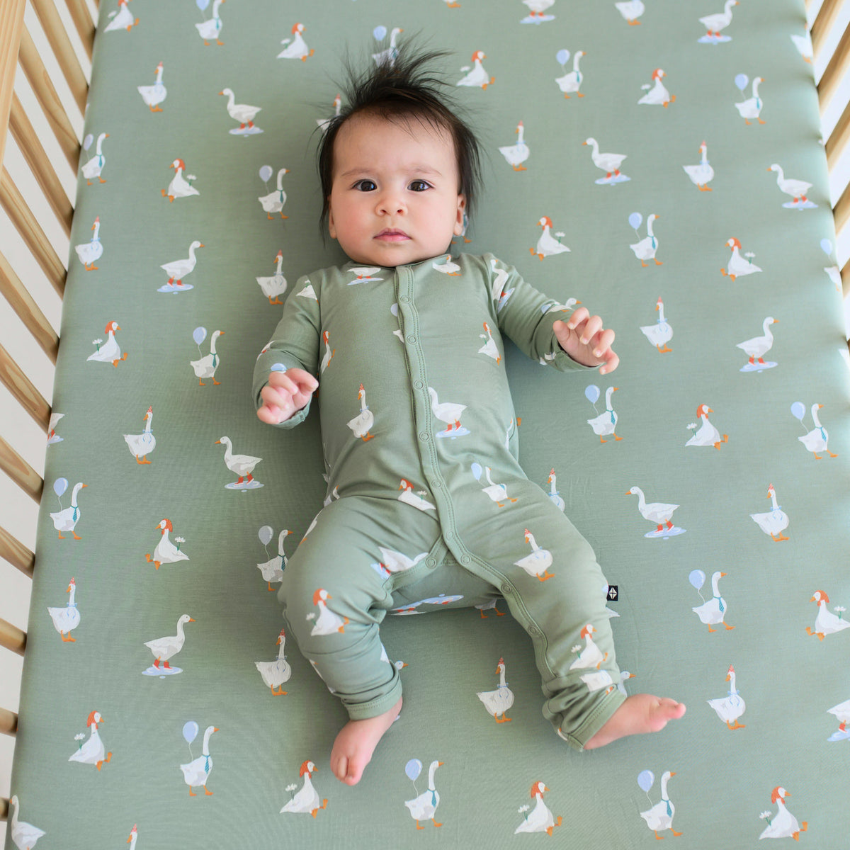 Infant laying in a crib on a Crib Sheet in Silly Goose wearing a matching snap romper