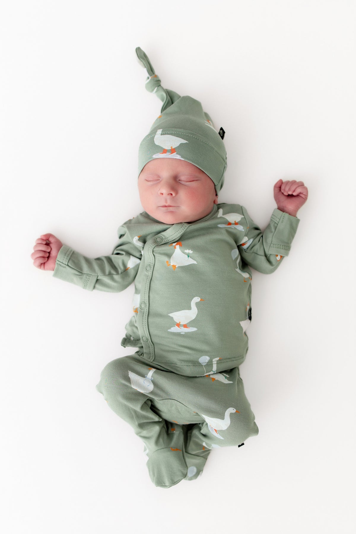 Newborn baby wearing a green outfit with silly goose patterns on a white background