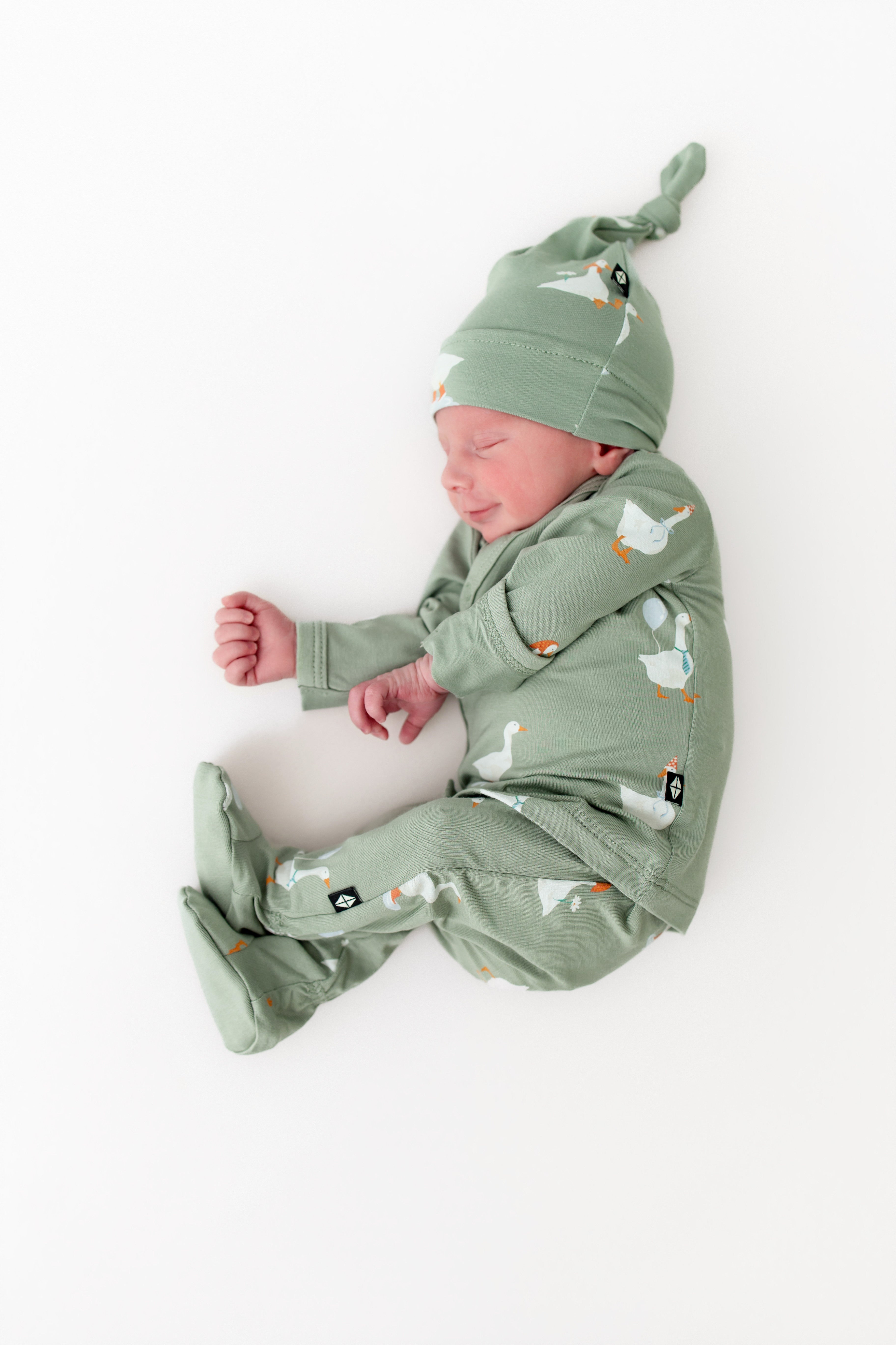 Newborn baby in a green outfit with silly goose pattern on a white background