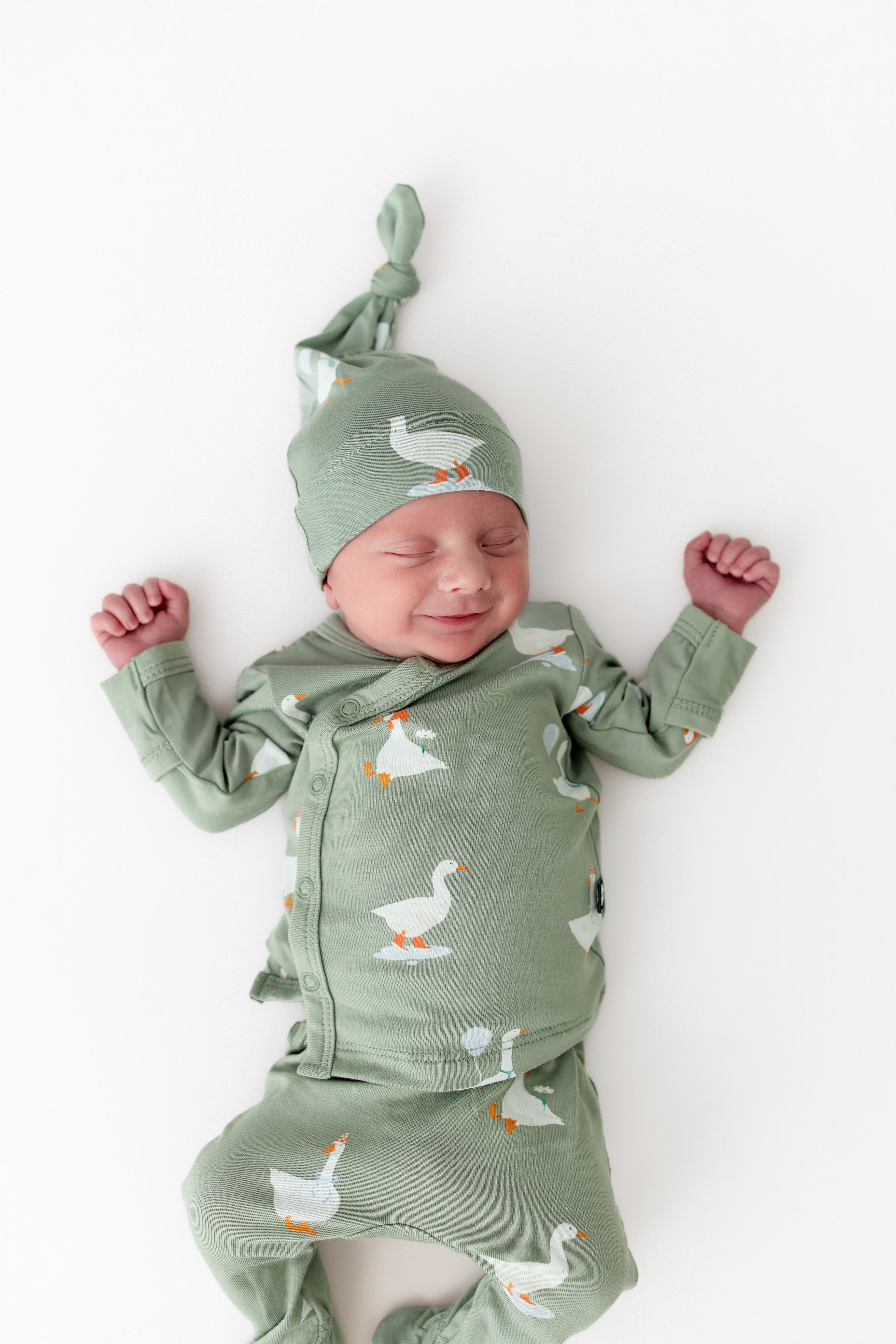 Newborn baby wearing a green outfit with silly goose pattern and matching hat on a white background