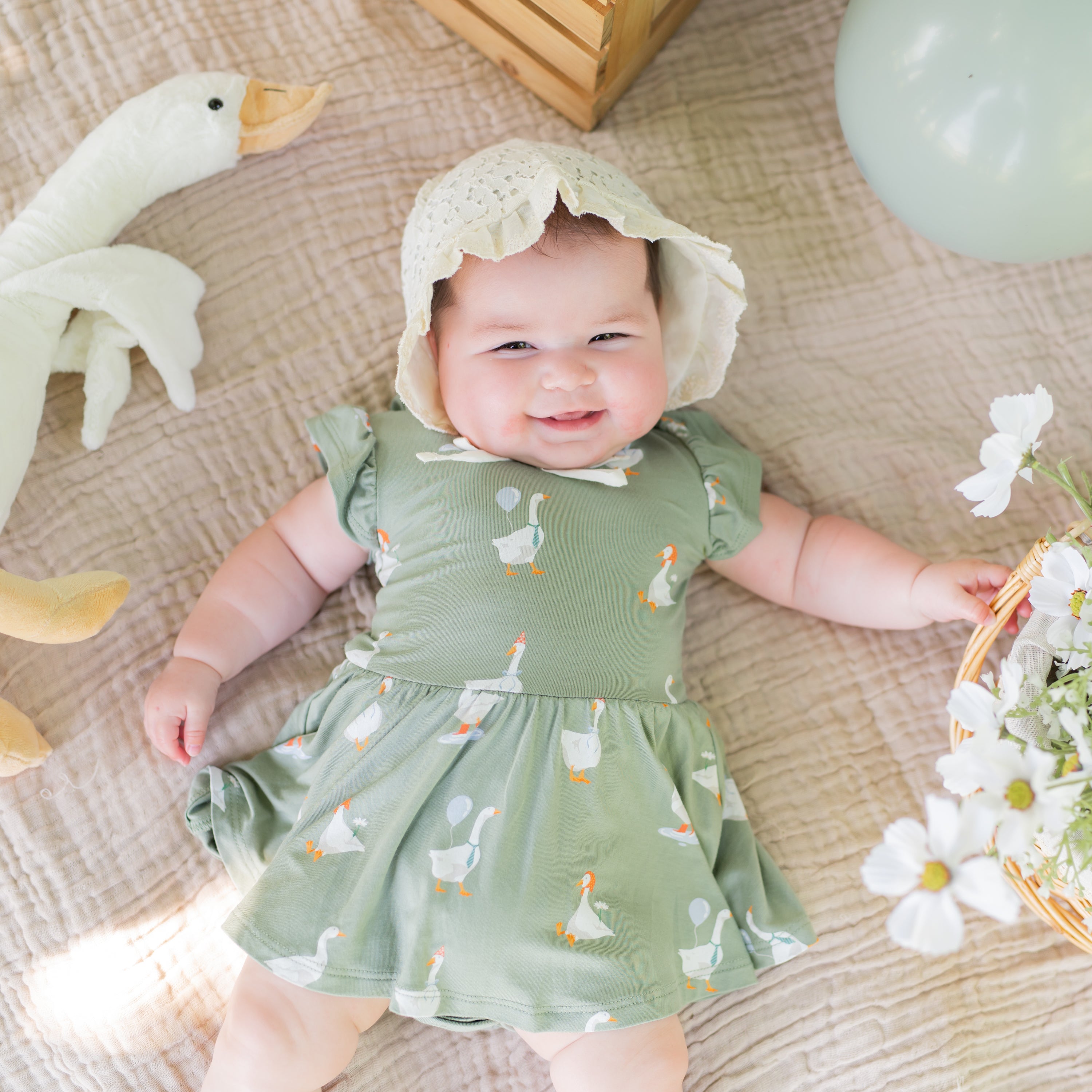 Close up of the Twirl Bodysuit Dress in Silly Goose shown on an infant model wearing a linen bonnet