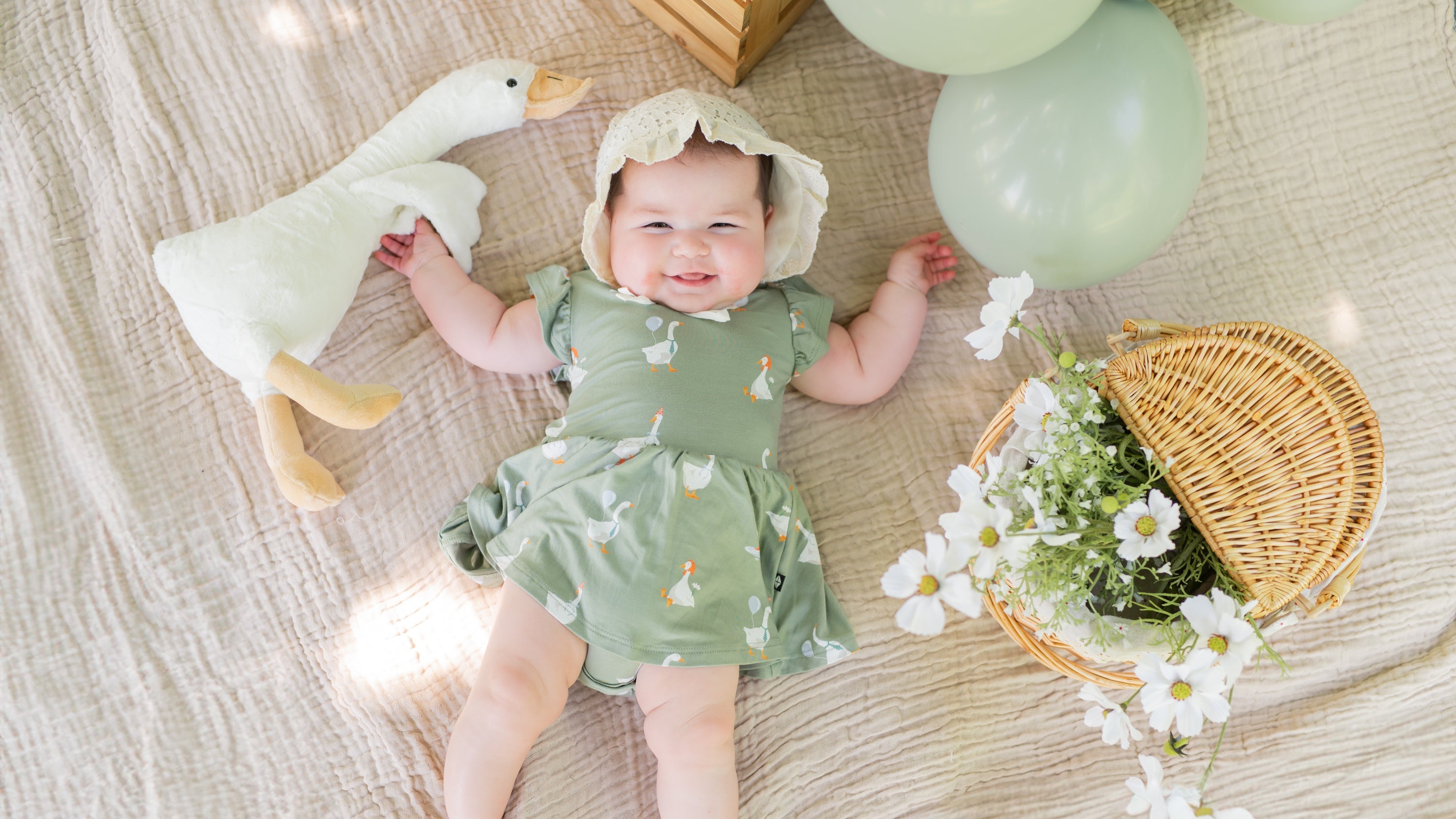 Baby in a twirl dress with a silly goose pattern laying on a picnic blanket