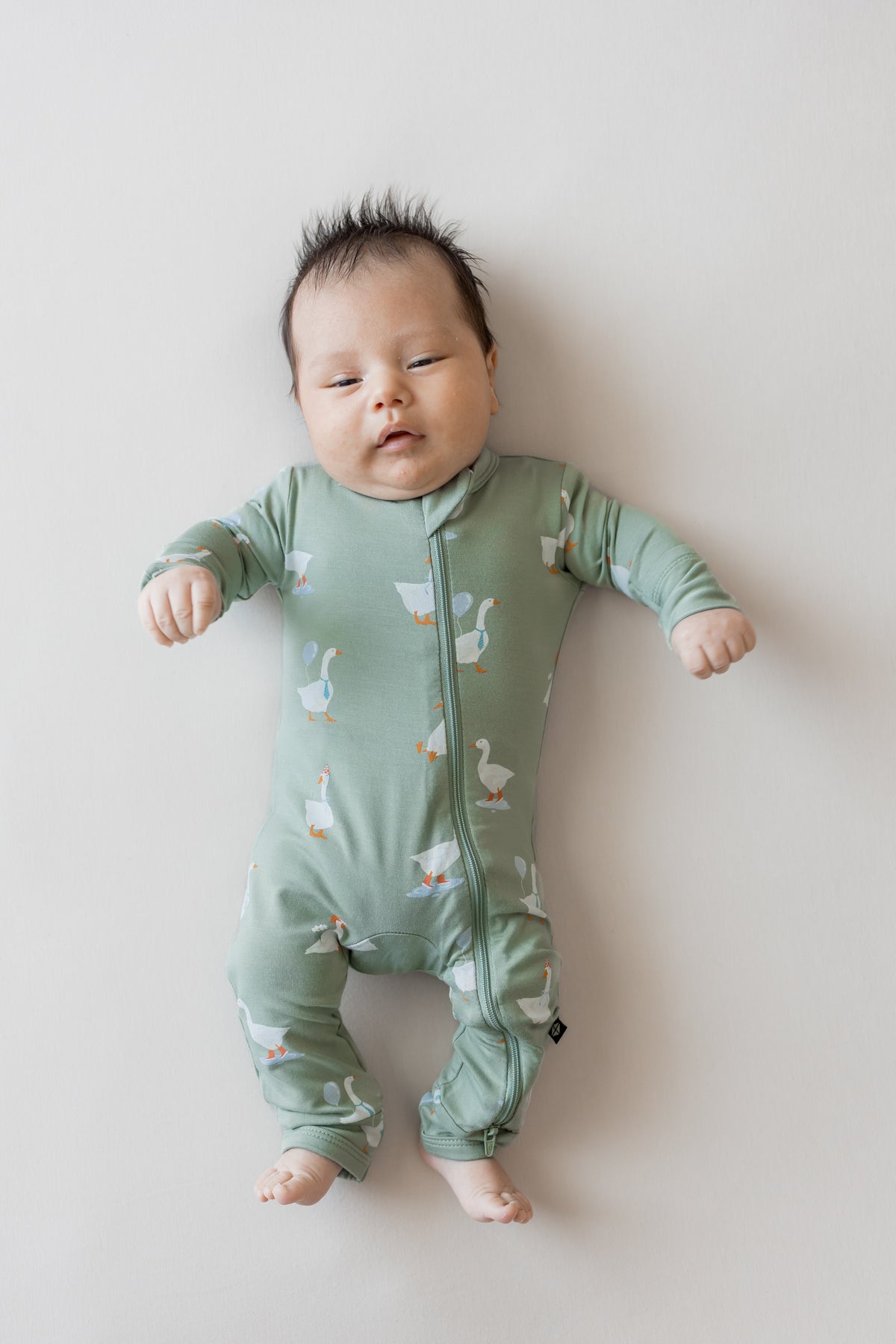 Baby wearing Zippered Romper in Silly Goose print on a beige background