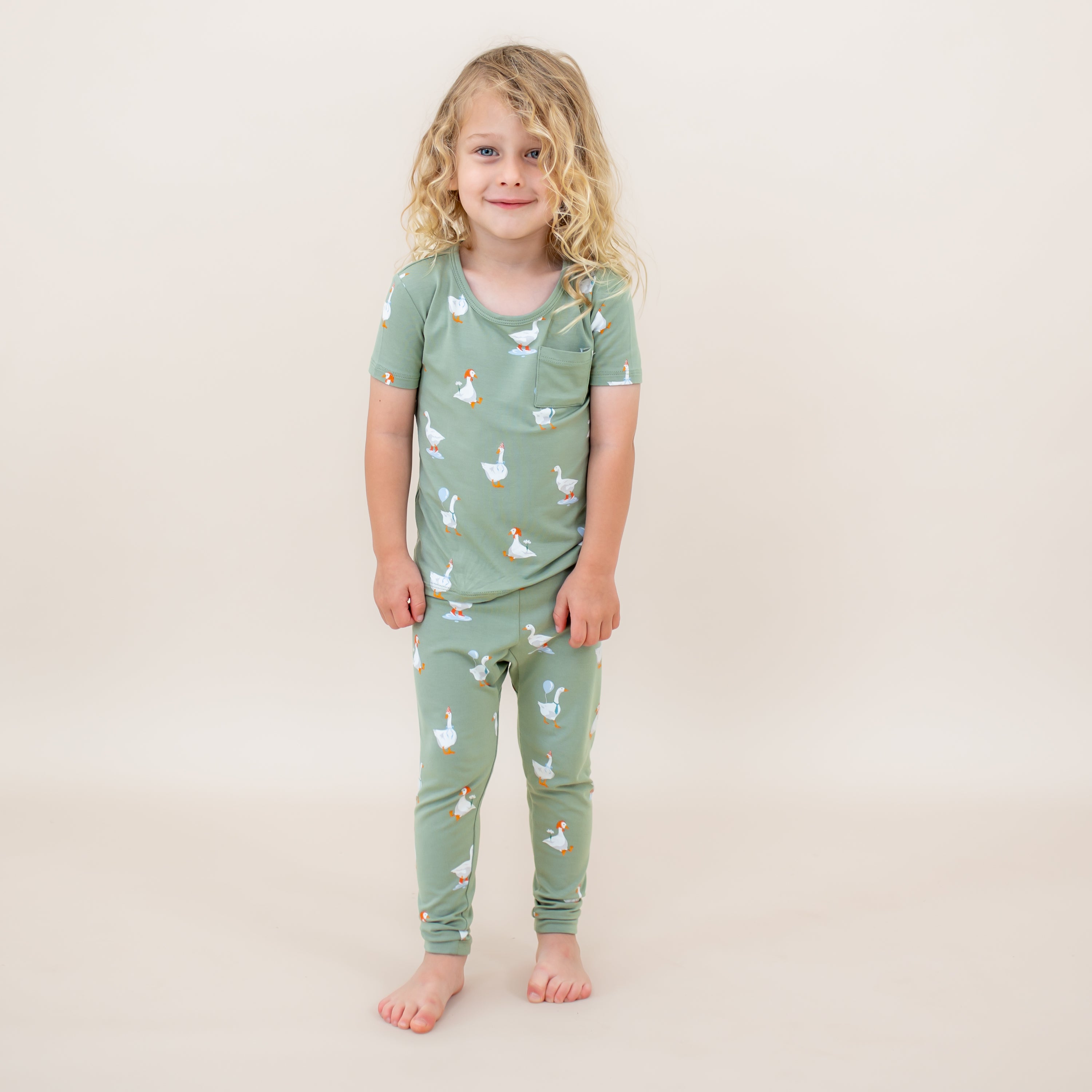Young child wearing the Short Sleeve with Pants Pajamas in Silly Goose standing in front of a light neutral backdrop