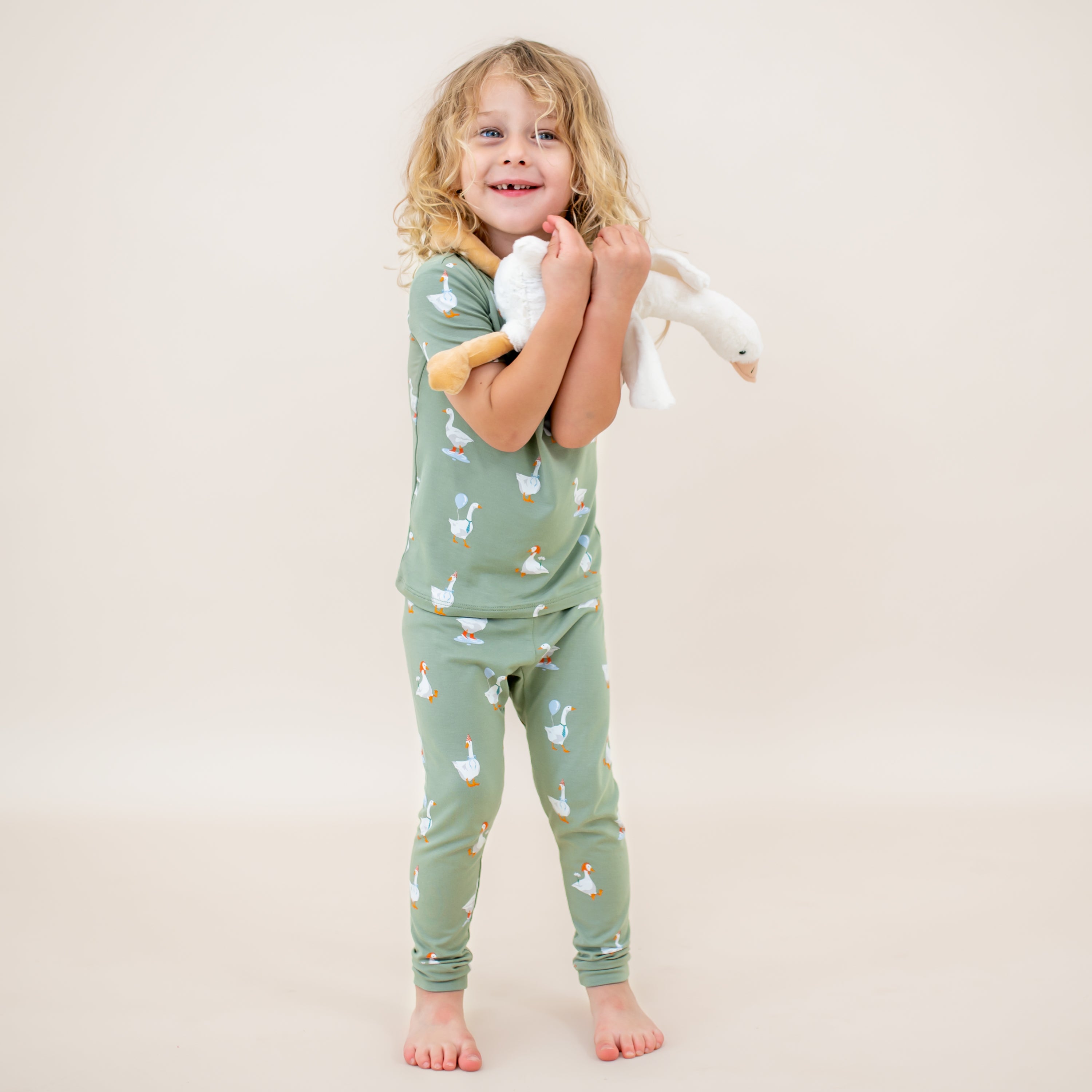 Young child standing holding a stuffed toy goose in front of them wearing the Short Sleeve with Pants Pajamas in Silly Goose