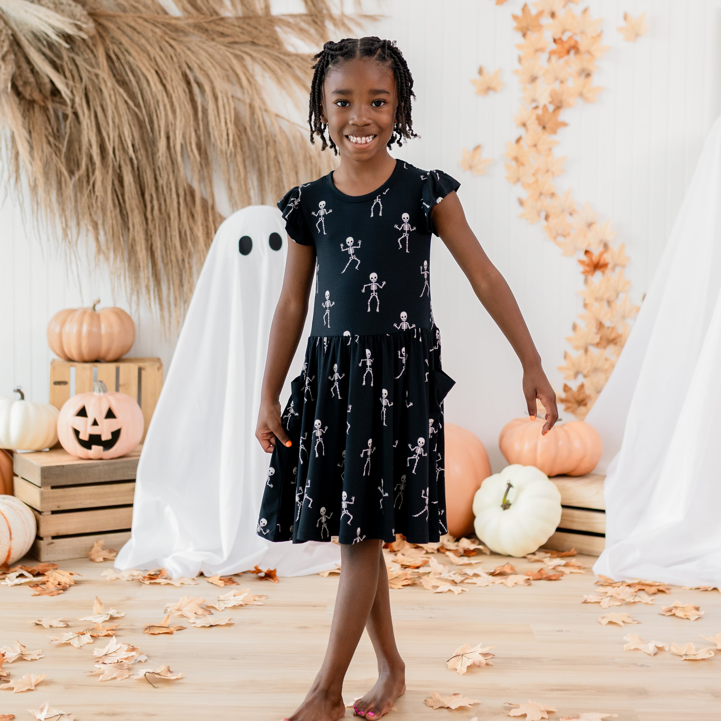 Smiling girl holding the side of her Pocket Dress in Skeleton in front of a fall backdrop