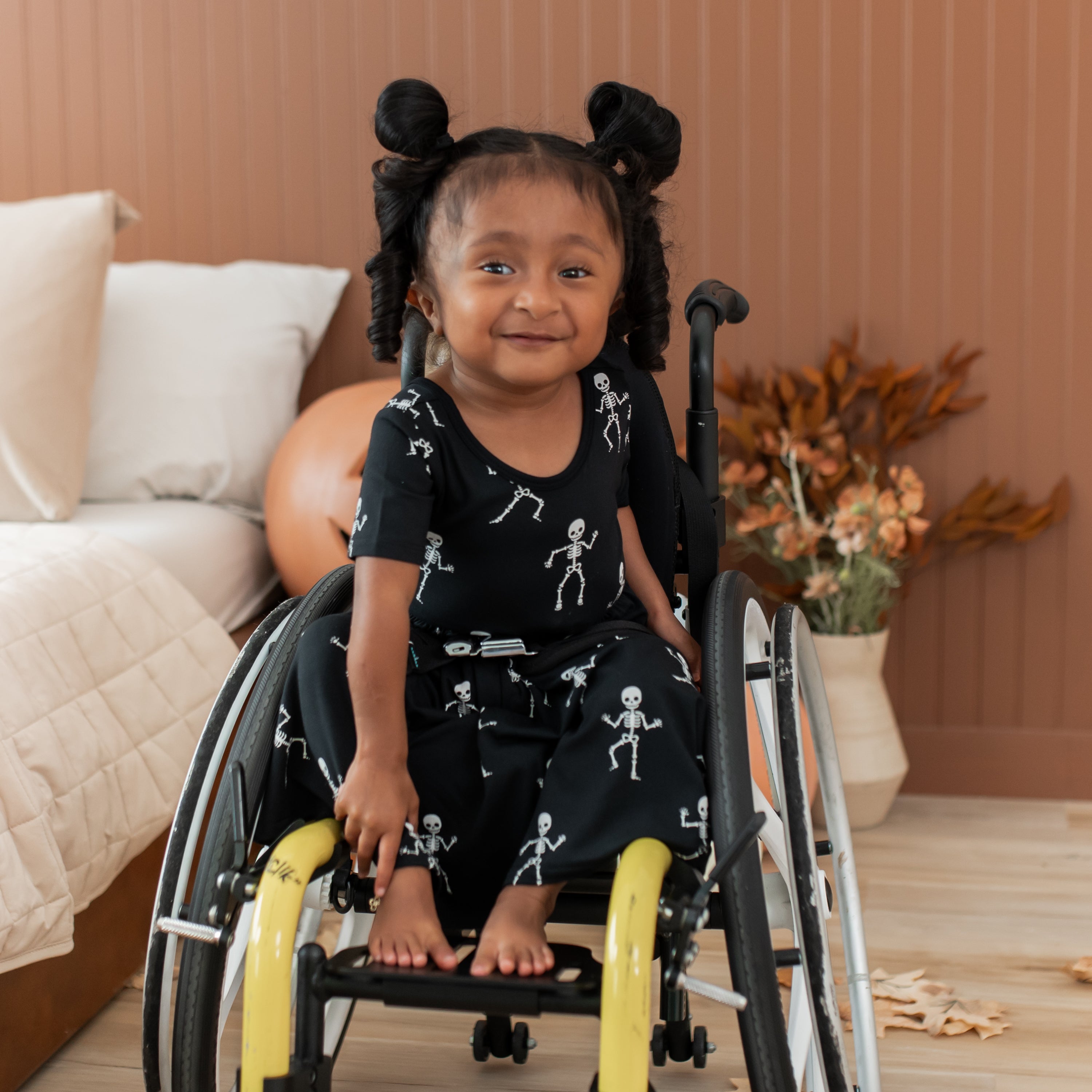 Child in a wheelchair with skeleton print dress in a cozy bedroom setting