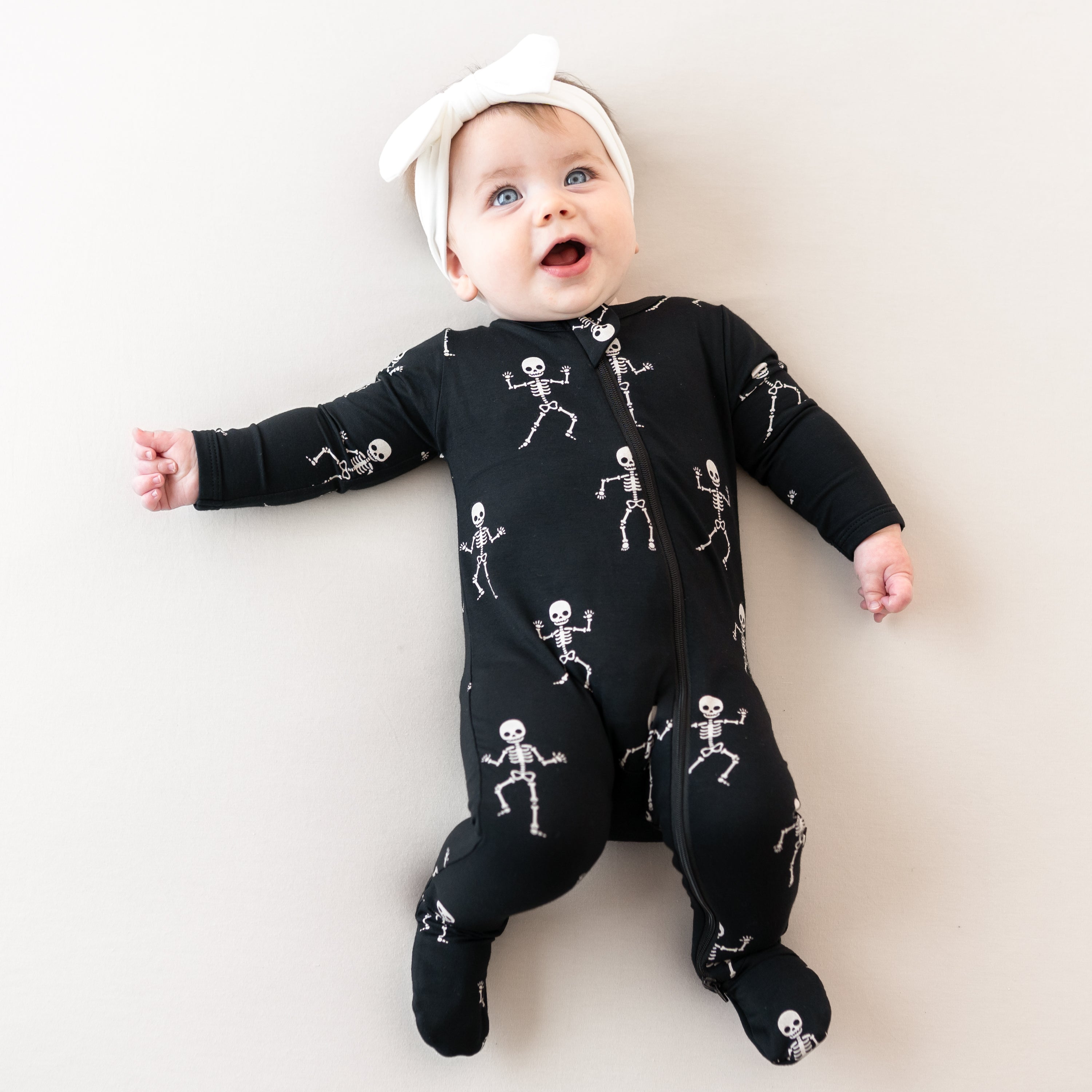 Baby wearing Zippered Footie Halloween pjs in Skeleton with Bow headband