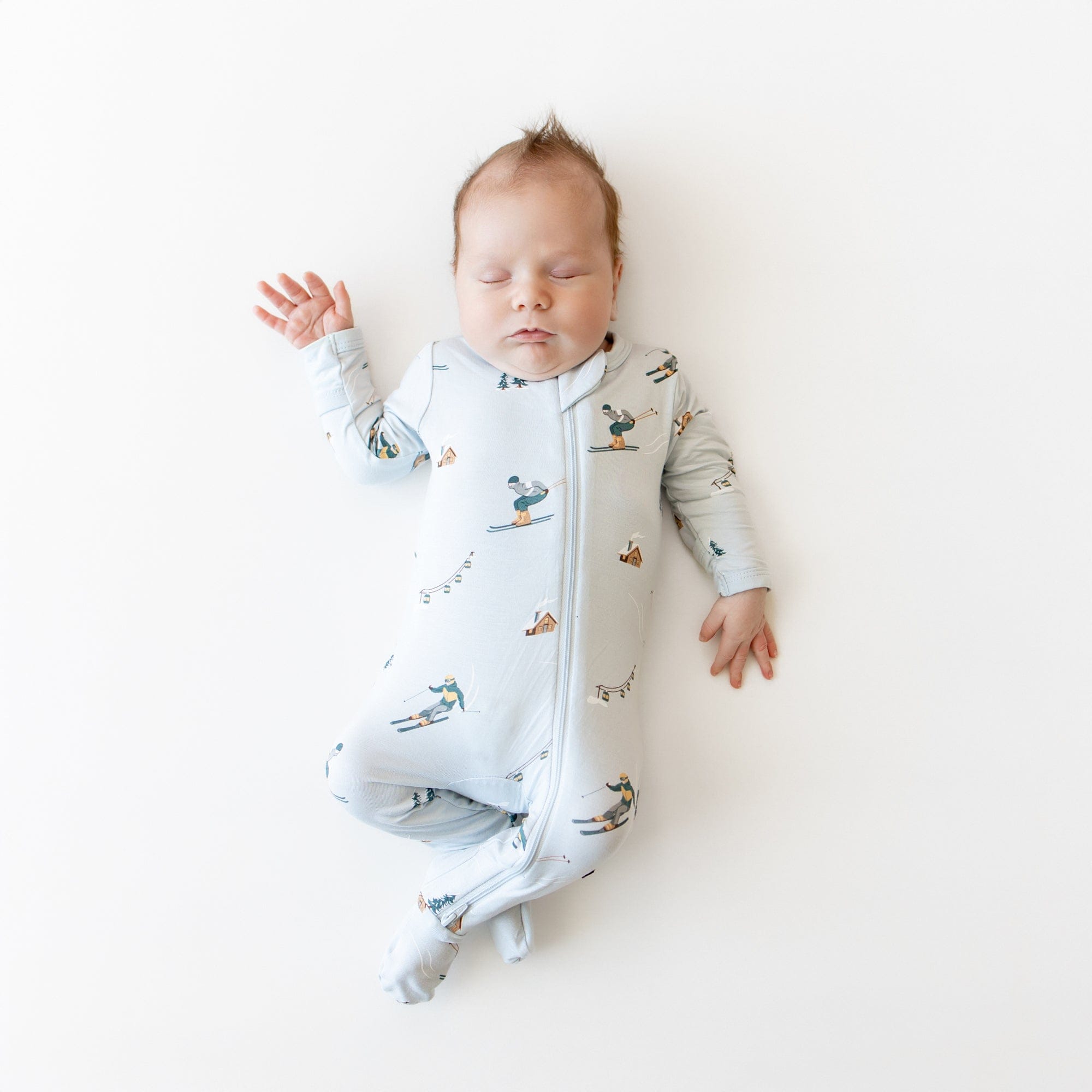 Sleeping infant on a light neutral surface wearing the Zippered Footie in Ski