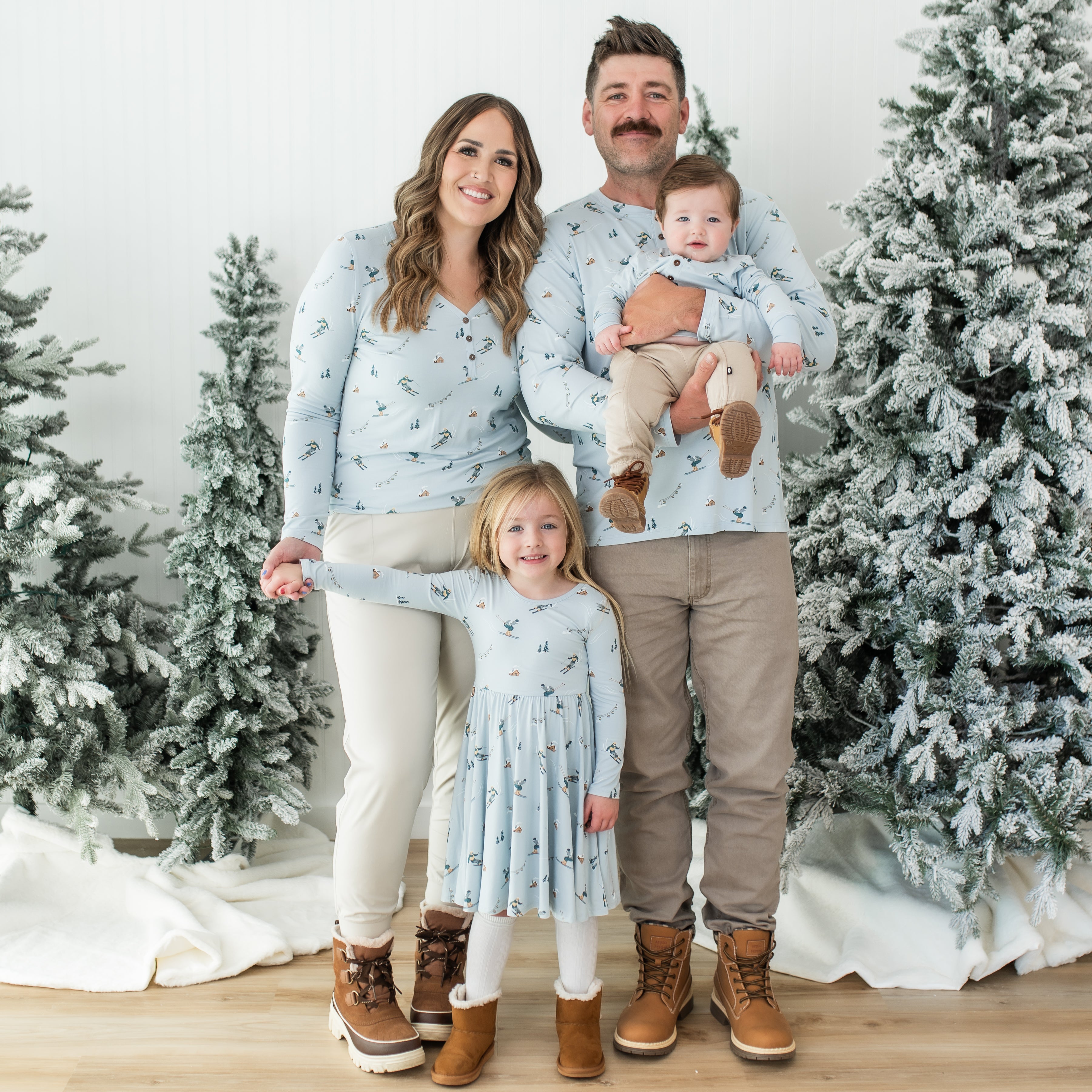 Family of four standing between two frosted trees matching in various items from the Ski collection