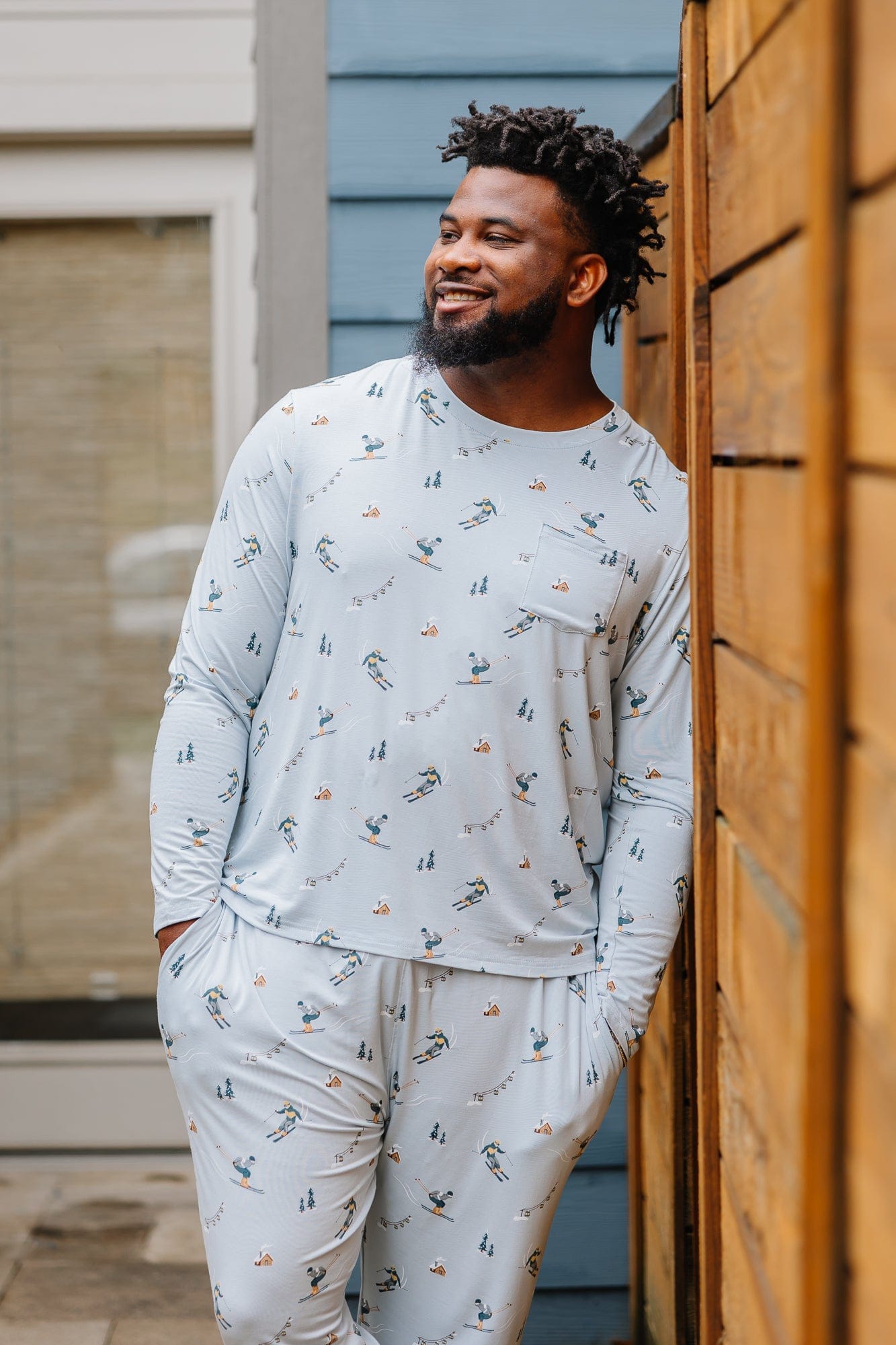 Smiling male model wearing the Men's Jogger Set in Ski looking off to the side leaning up against a fence