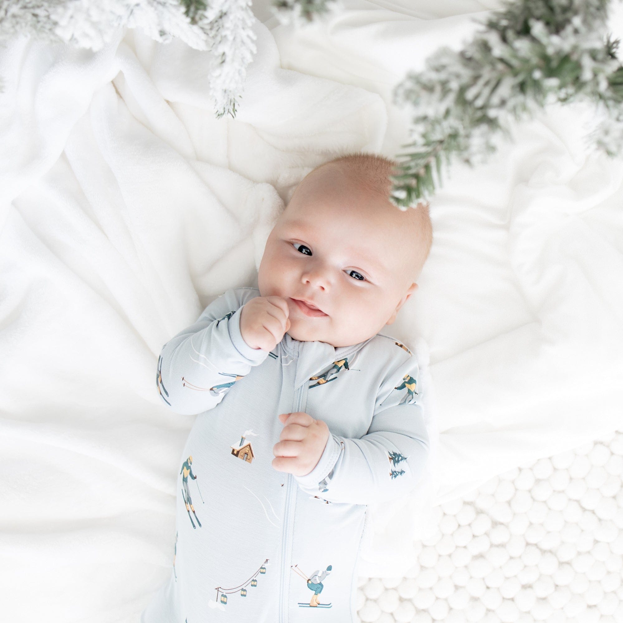 Close up of the Zippered Romper in Ski shown on an infant who is lying on the floor on top of a white blanket