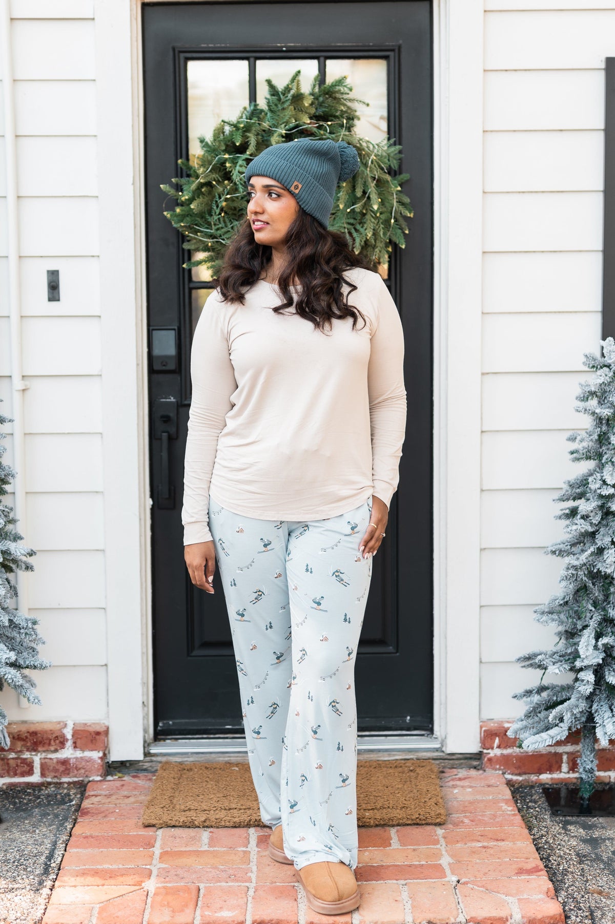 Female model standing at a front door wearing the Women's Lounge Pants in Ski paired with a cream colored shirt and Atlantic beanie
