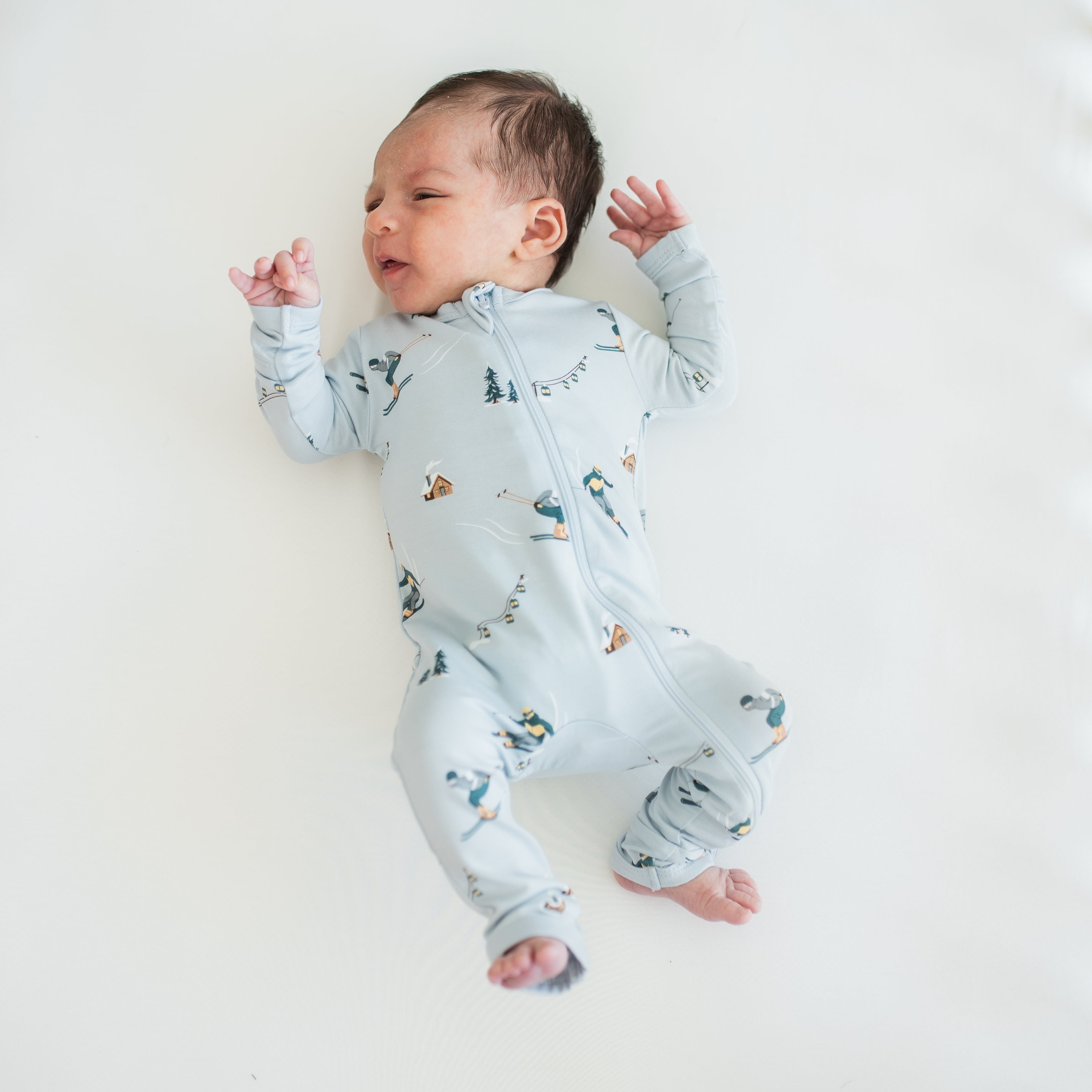 Newborn laying on a light colored surface wearing the Zippered Romper in Ski
