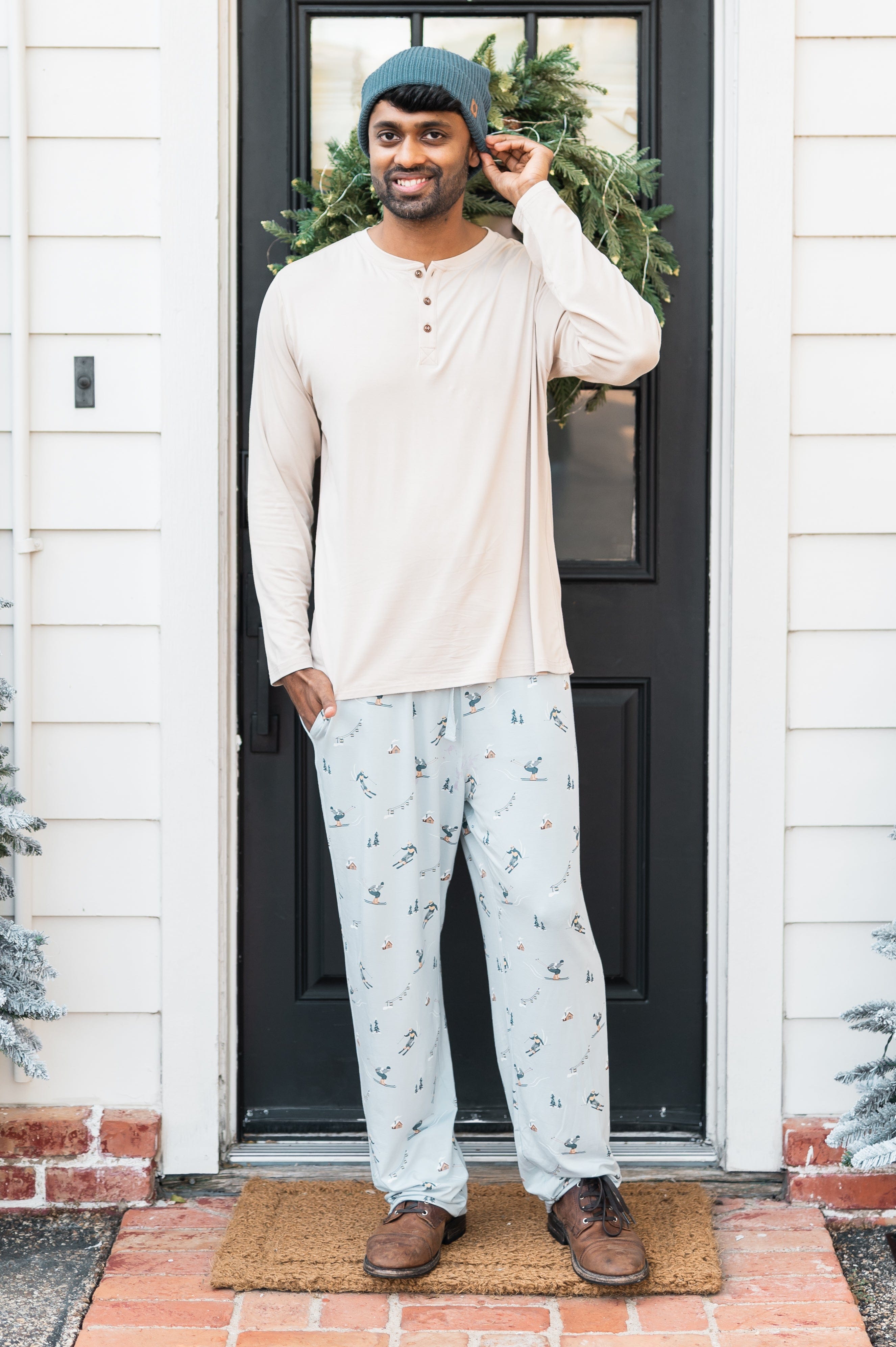 Male model standing at a front door wearing the Men's Lounge Pants in Ski paired with a cream shirt and Atlantic beanie
