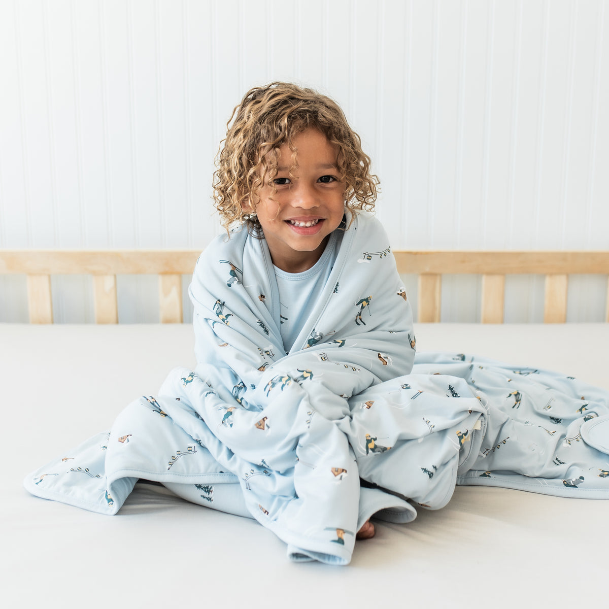 Young boy sitting on a bed with the Toddler Blanket in Ski 1.0 wrapped around him