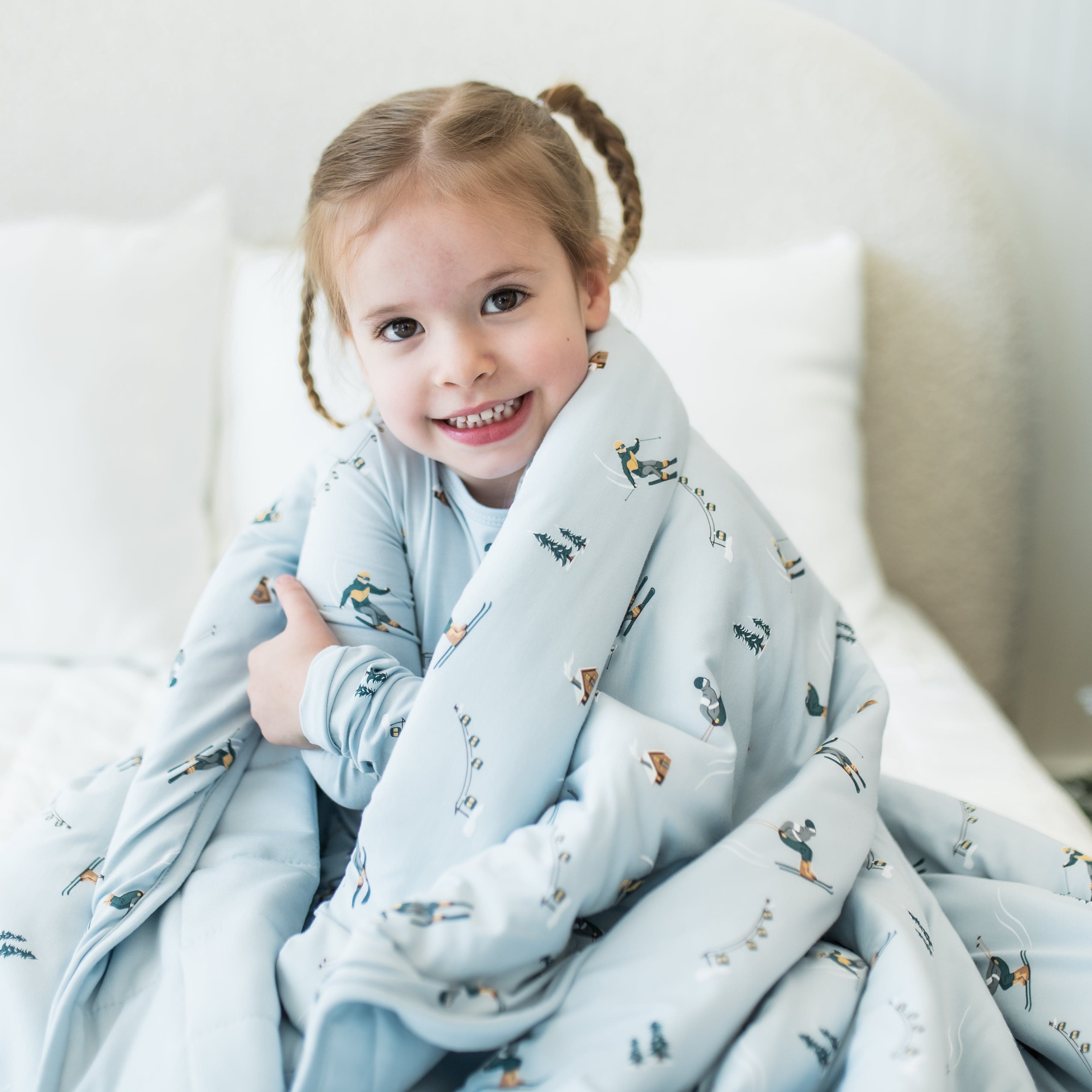 Close up of smiling girl sitting on a bed with the Youth Blanket in Ski 2.5 wrapped around her