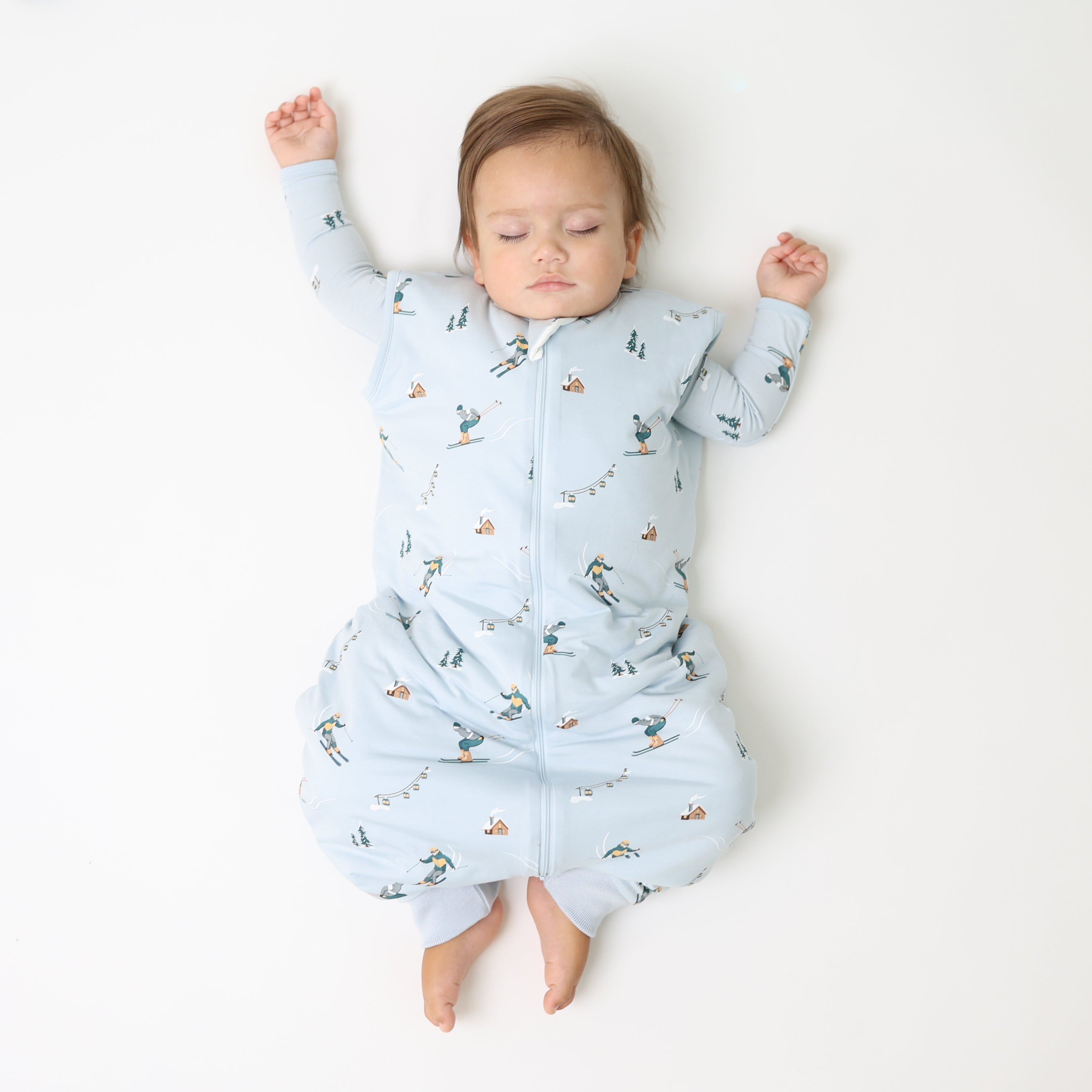 Toddler laying on a light neutral surface wearing the Sleep Bag Walker in Ski 1.0 with a matching long sleeve romper on underneath
