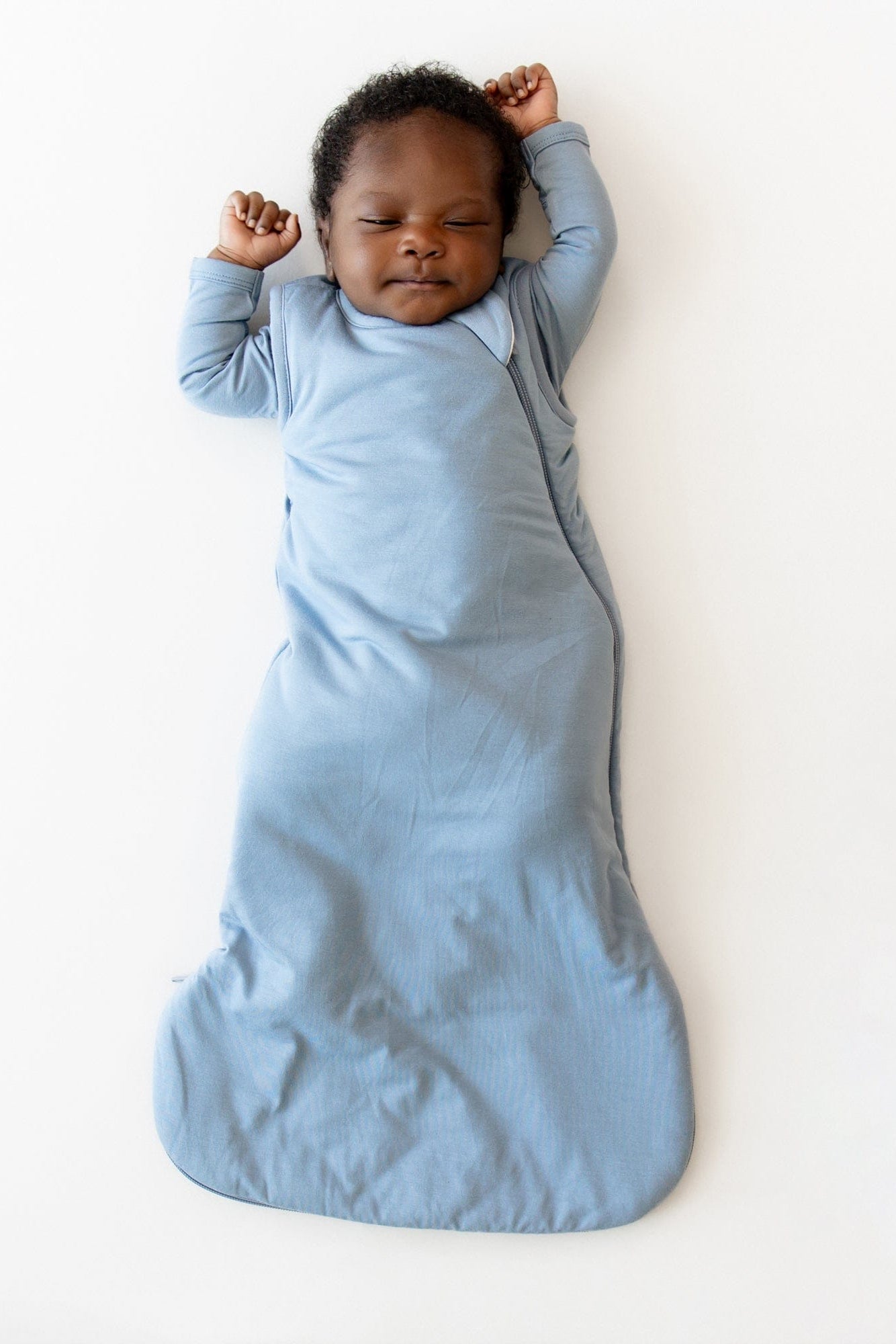Baby sleeping in a blue sleep bag on a white background