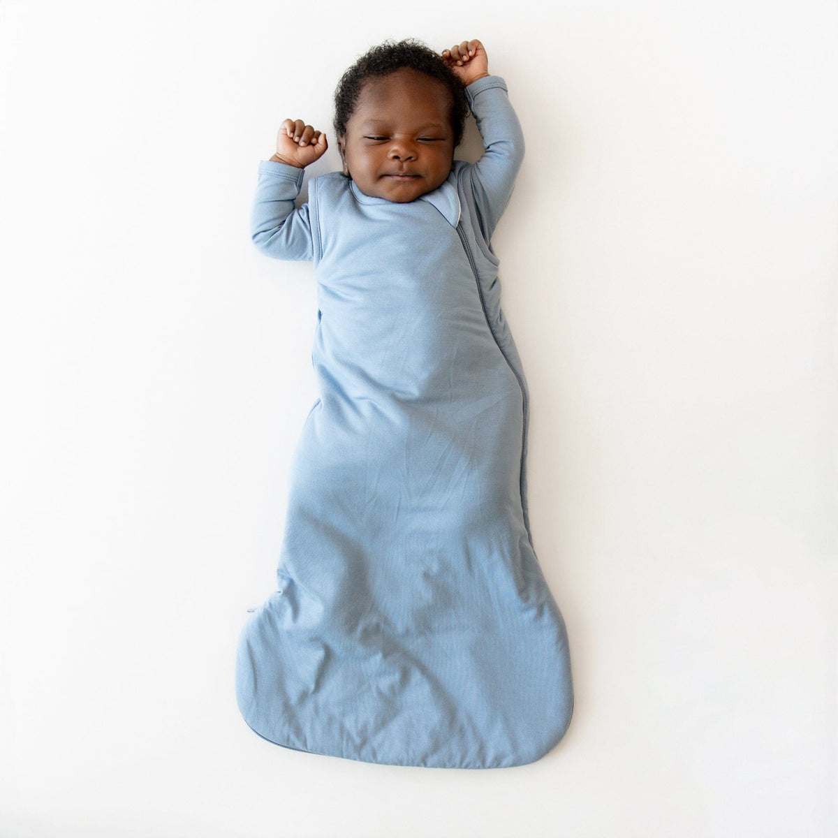 Baby sleeping in a blue sleep bag on a white background