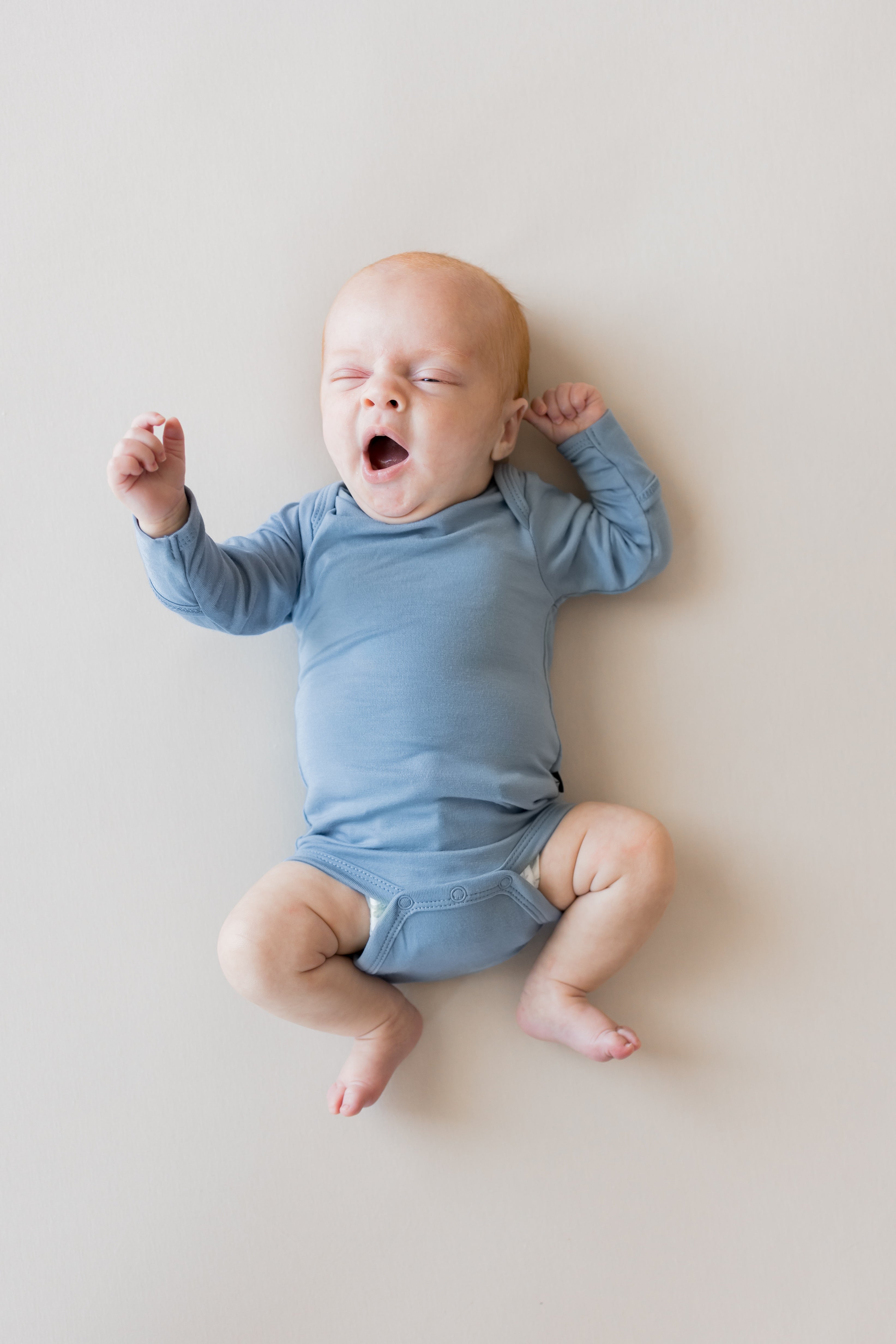Baby yawning in Long Sleeve Bodysuit in Slate color on a beige background