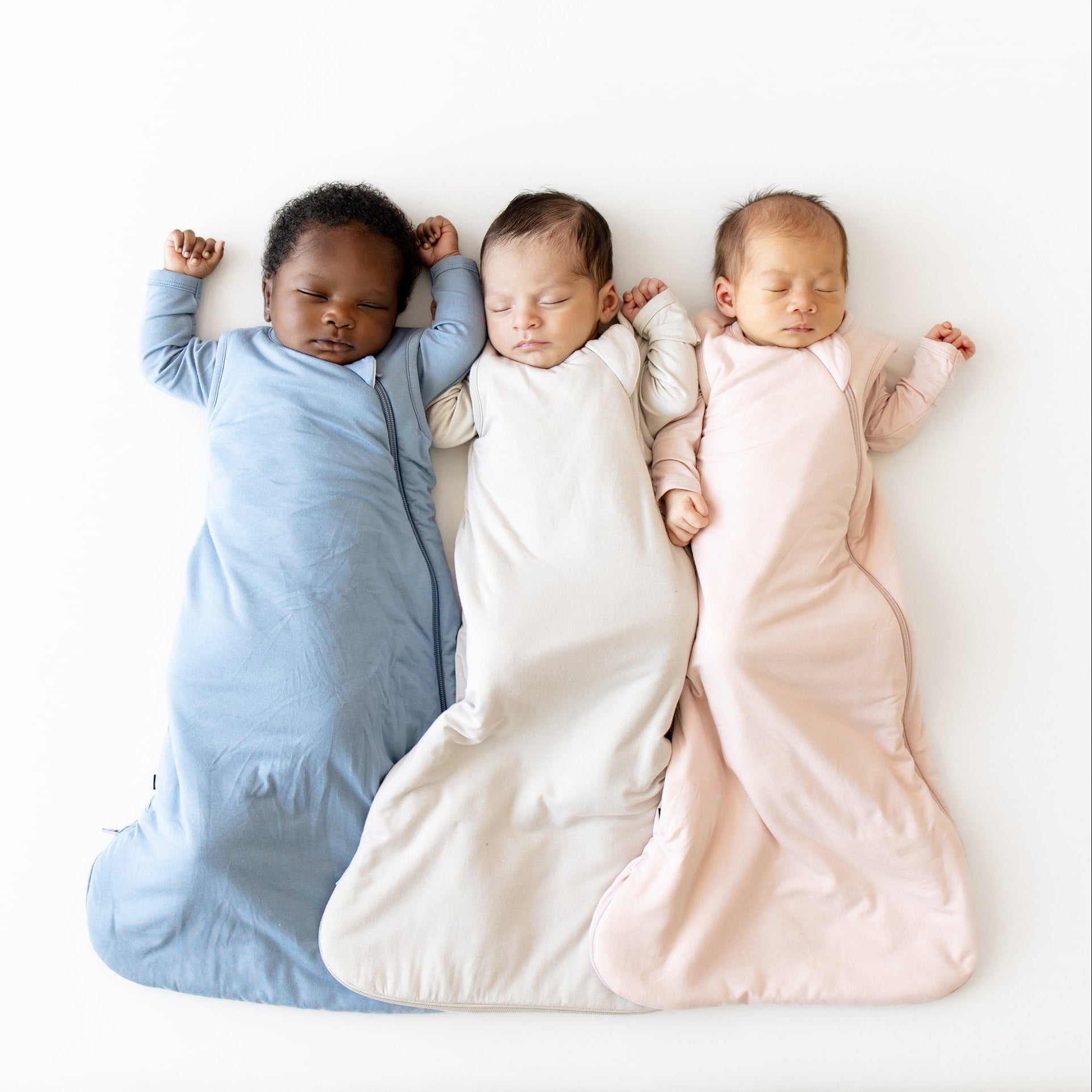 Three babies in colorful sleep bags lying on a white surface