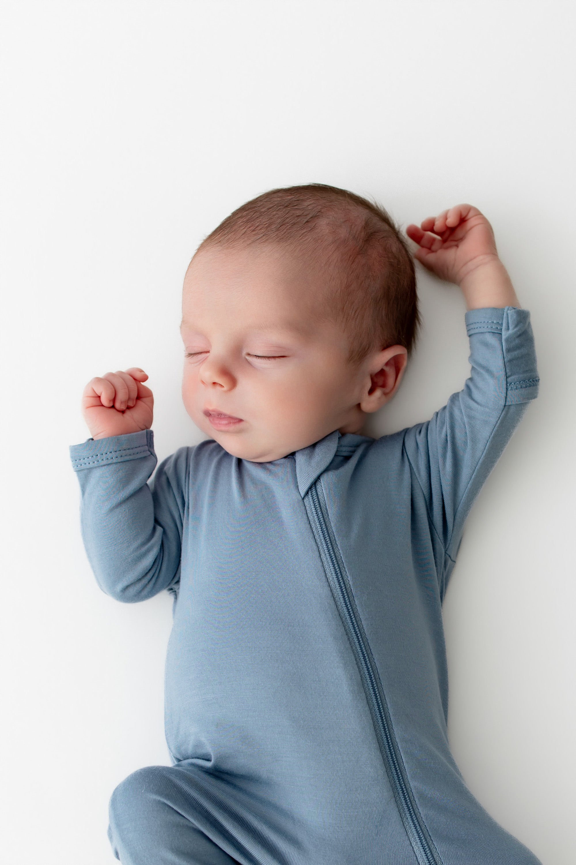 Newborn baby in a blue footie pajama lying on a white surface