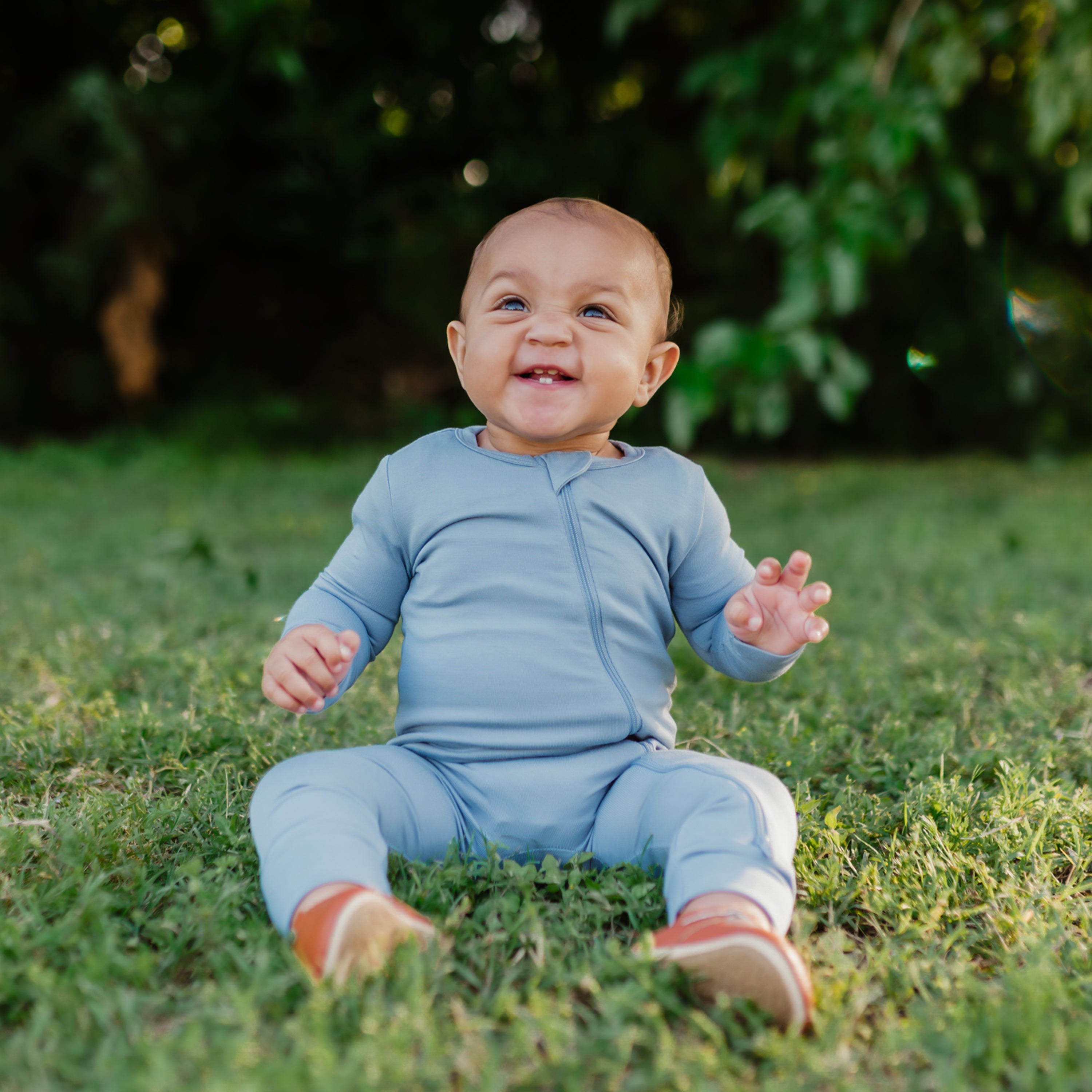Smiling baby sitting in the grass while wearing a Zippered Romper in Slate