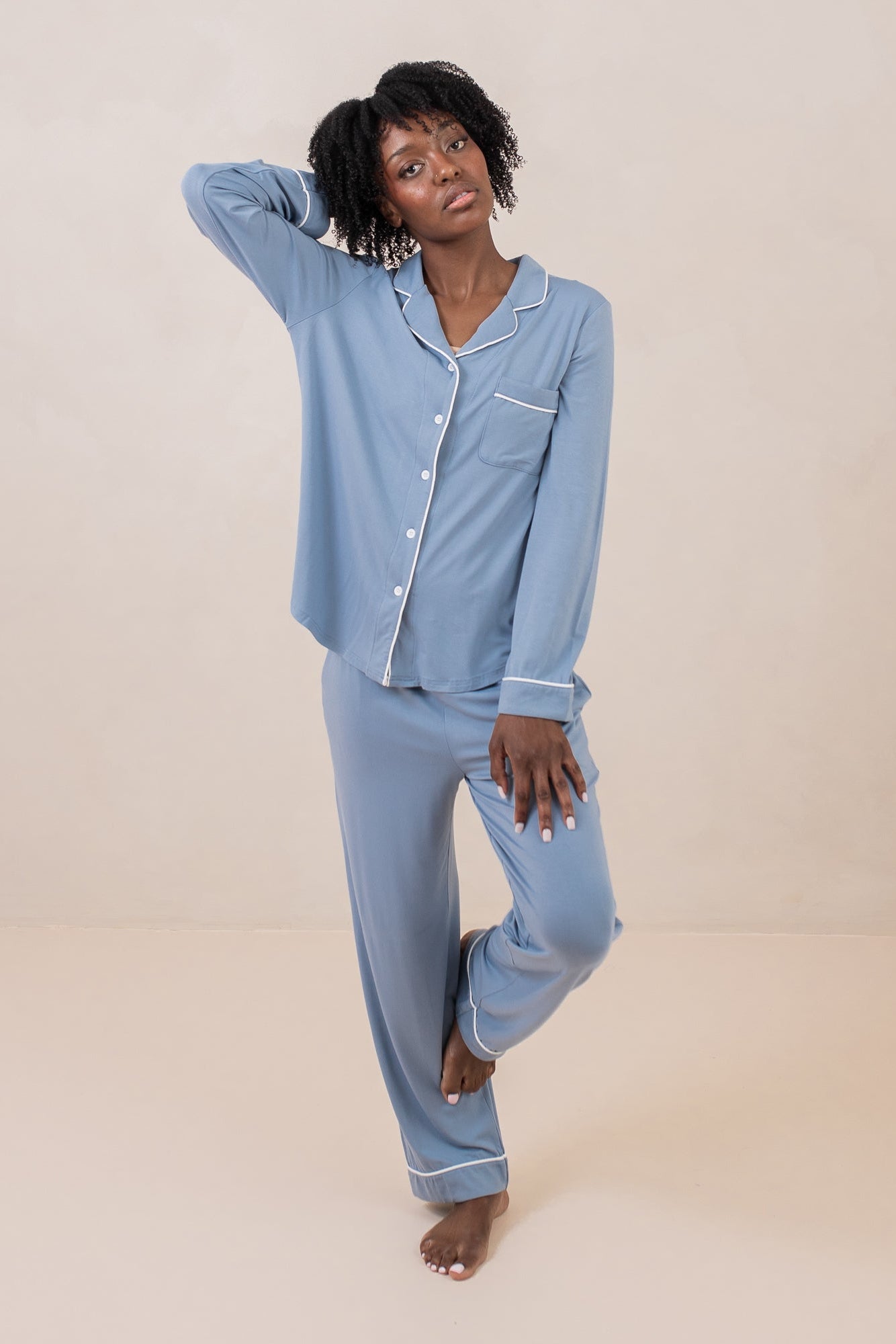 Female model standing on one leg with the other leg resting on her calf wearing the Long-Sleeved Women's Pajama Set in Slate with Cloud Trim