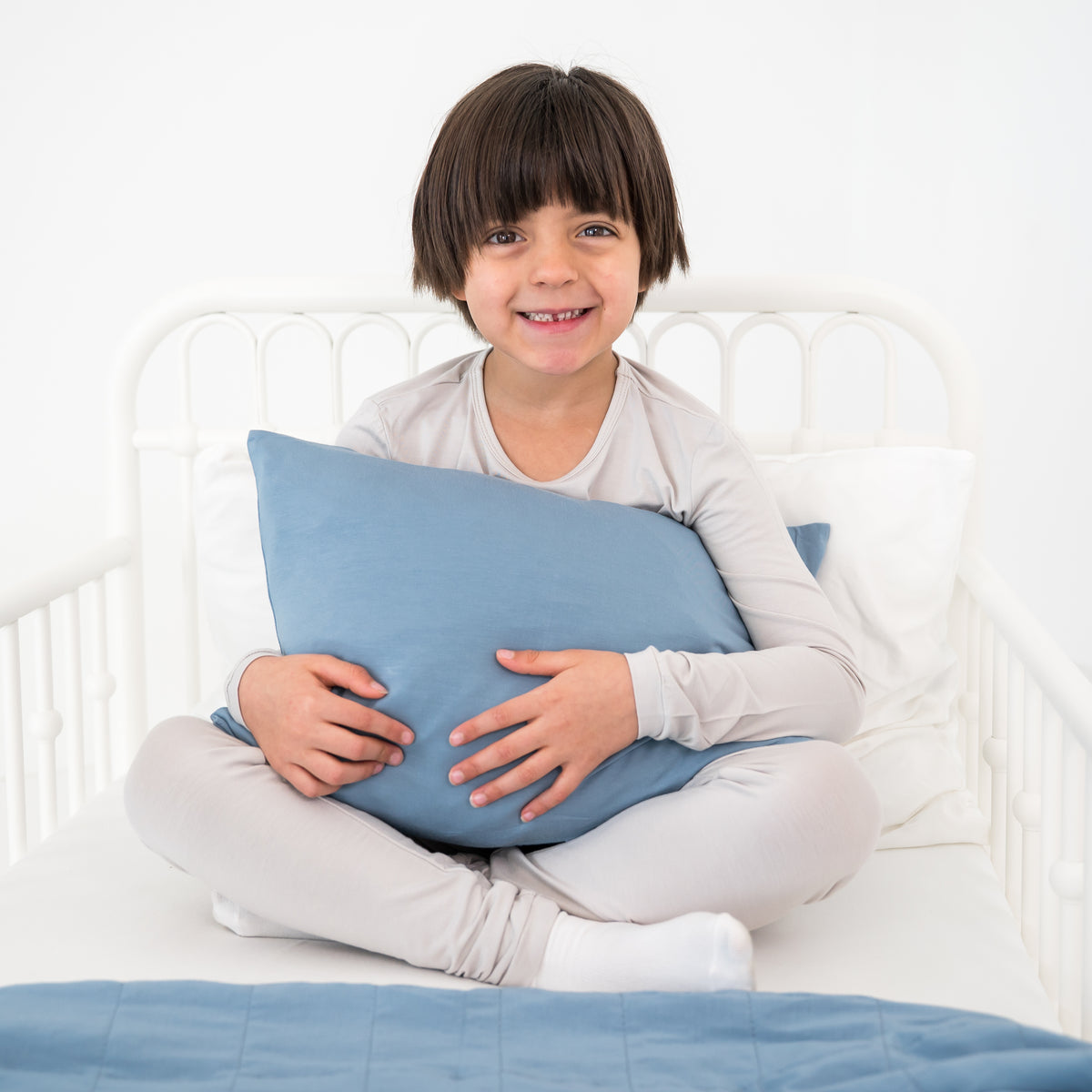 Toddler holding a blue pillow on a white bed