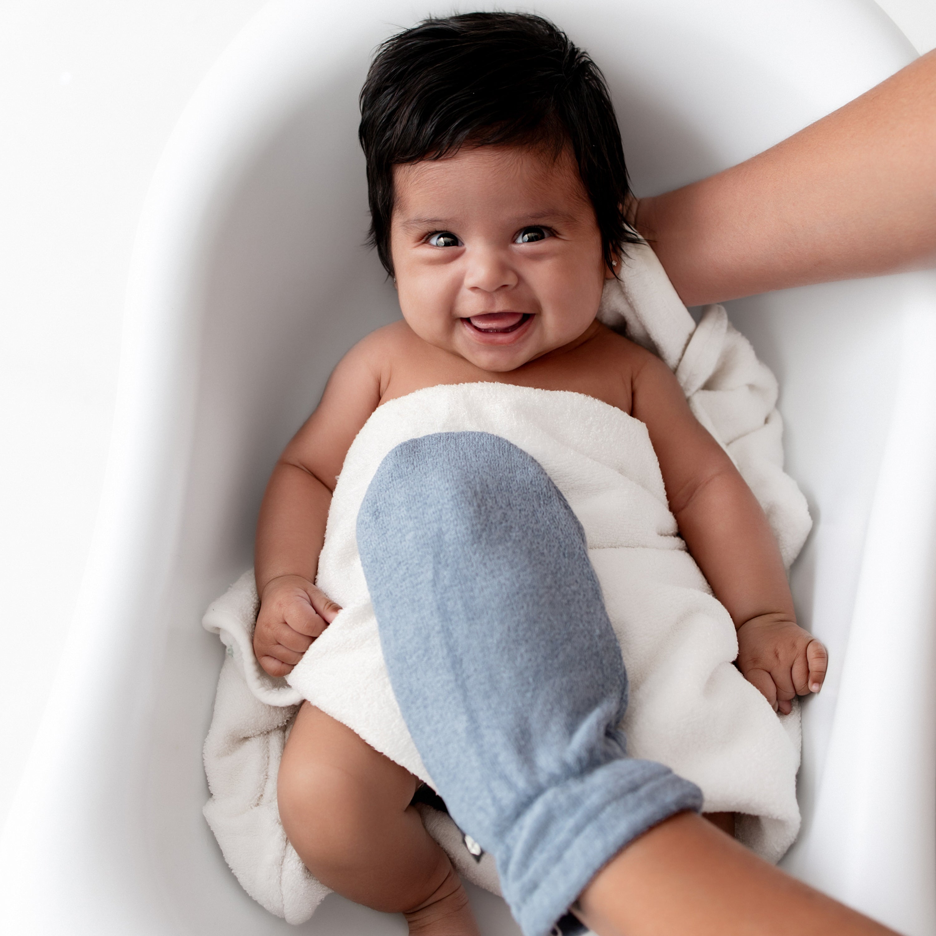 Infant girl in an infant tub wearing a white towel with a Terry Bath Mitt in Slate resting on her chest