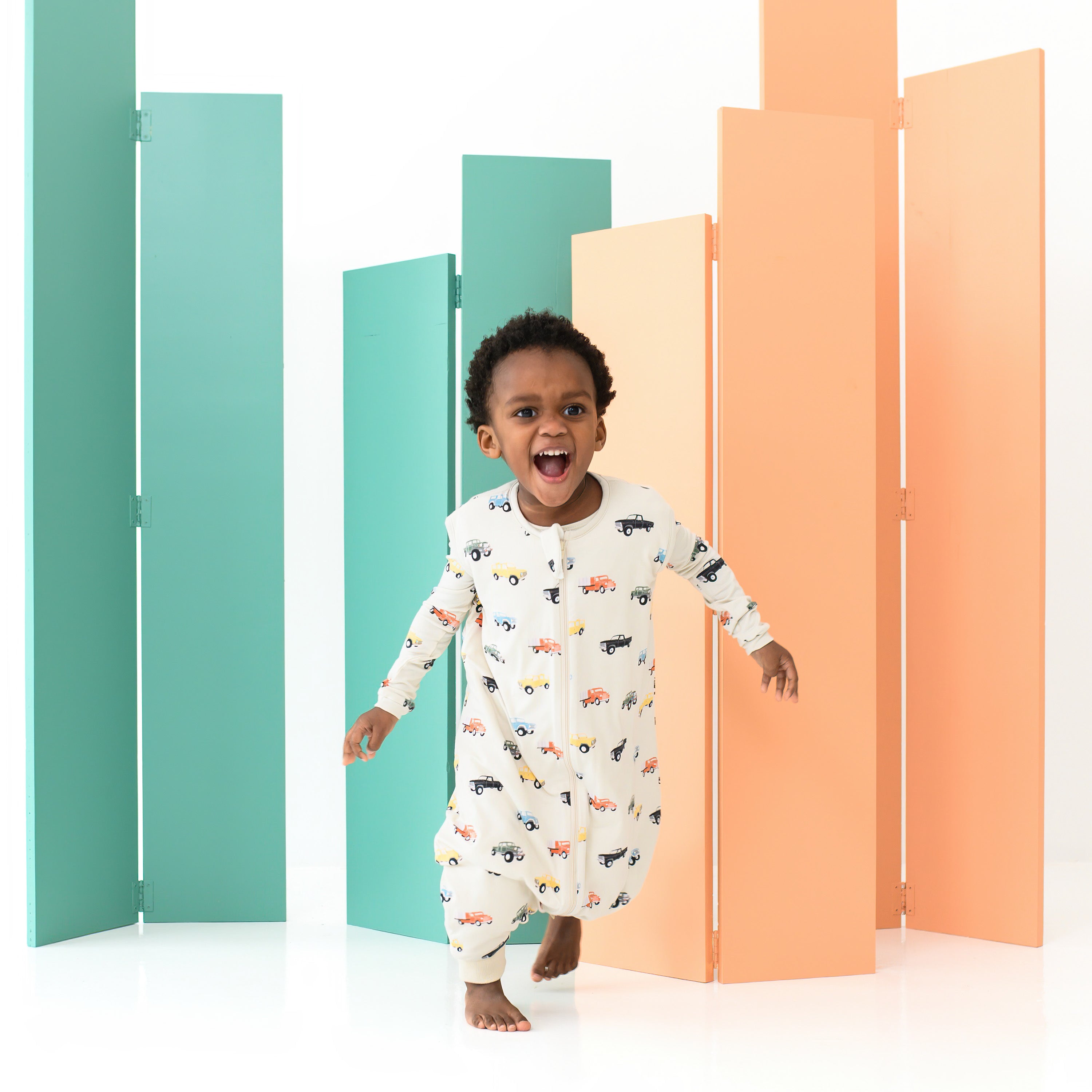 Laughing toddler walking forward wearing the Sleep Bag Walker in Vintage Truck 1.0