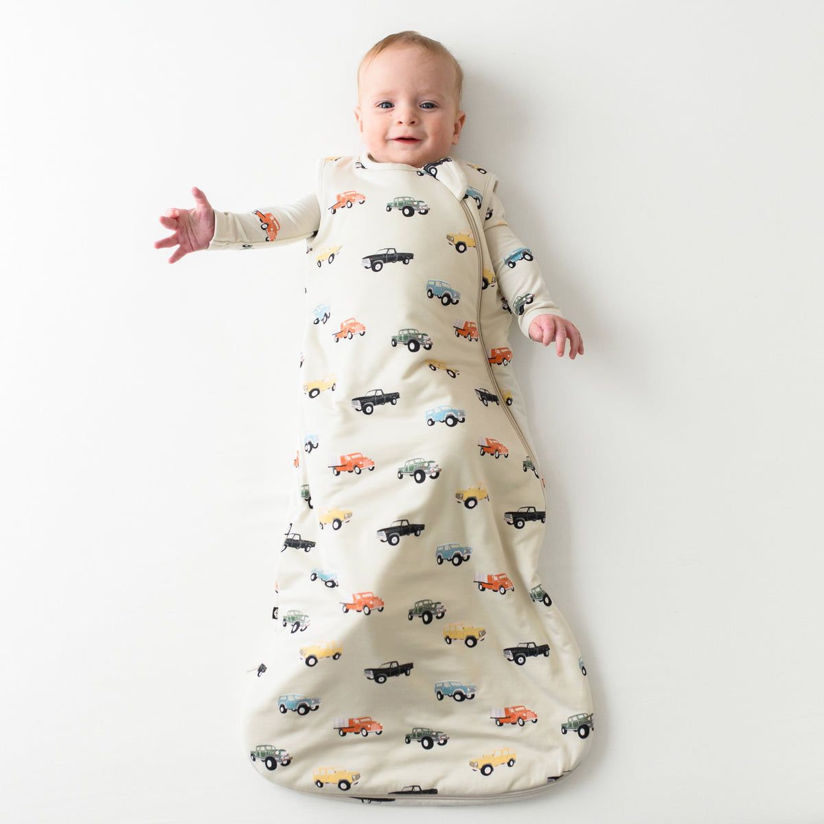Smiling baby wearing the 1.0 Vintage Truck Sleep Bag with a Vintage Truck long sleeve romper on underneath