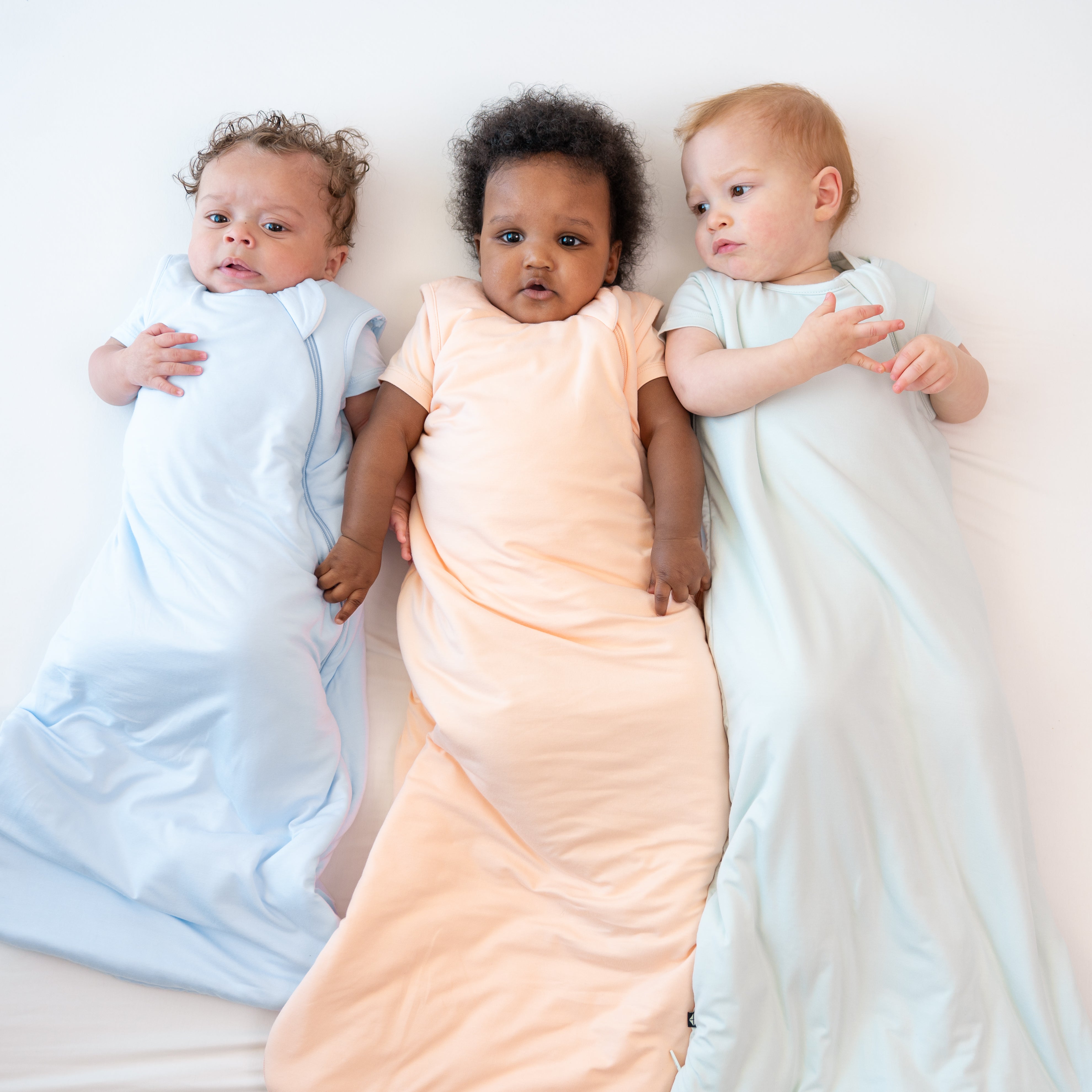 Three infant models wearing the 1.0 TOG Sleep Bags in Summer Solid colors