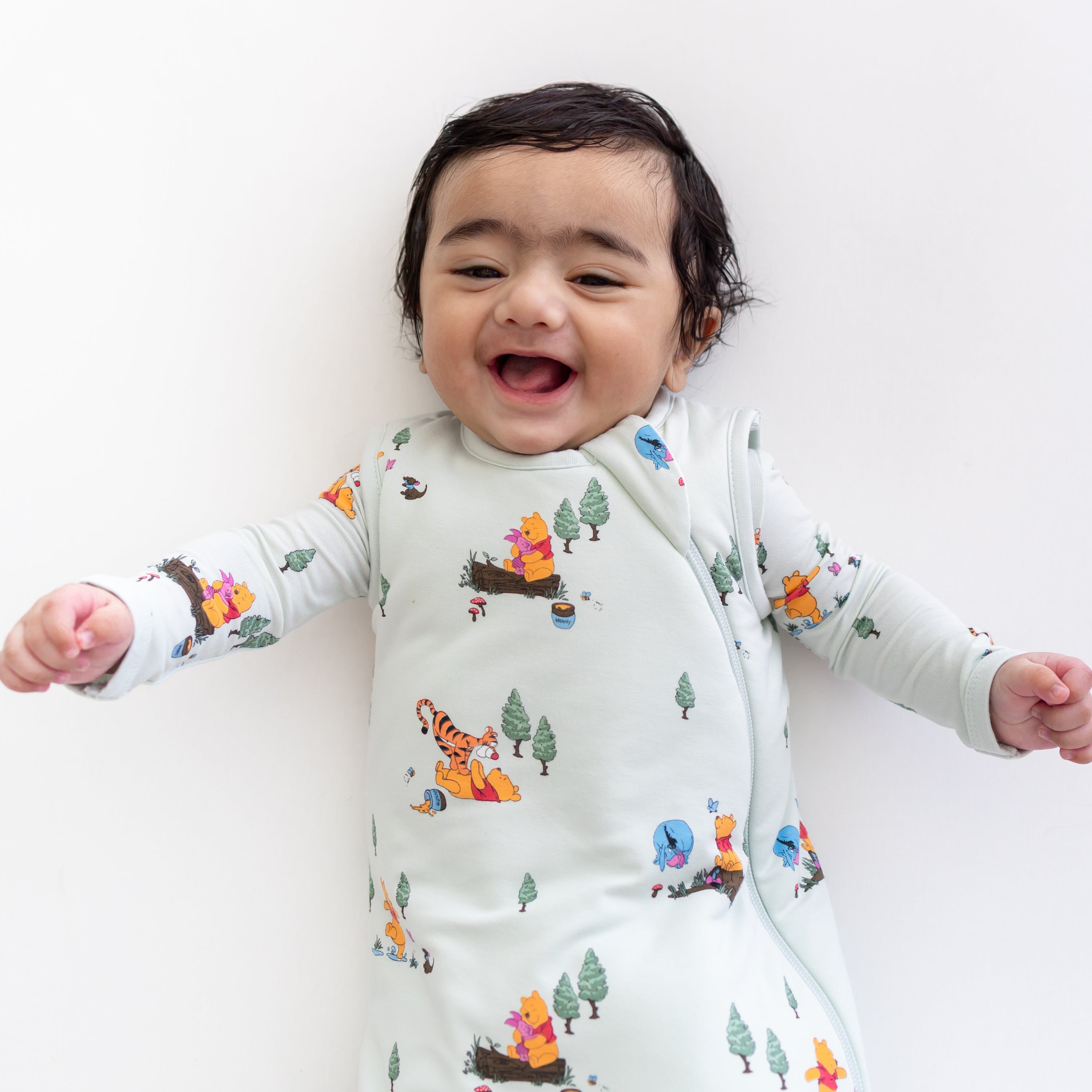Close up of an infant wearing the Sleep Bag in Winnie the Pooh Hundred Acre Wood 1.0 with a matching romper on underneath