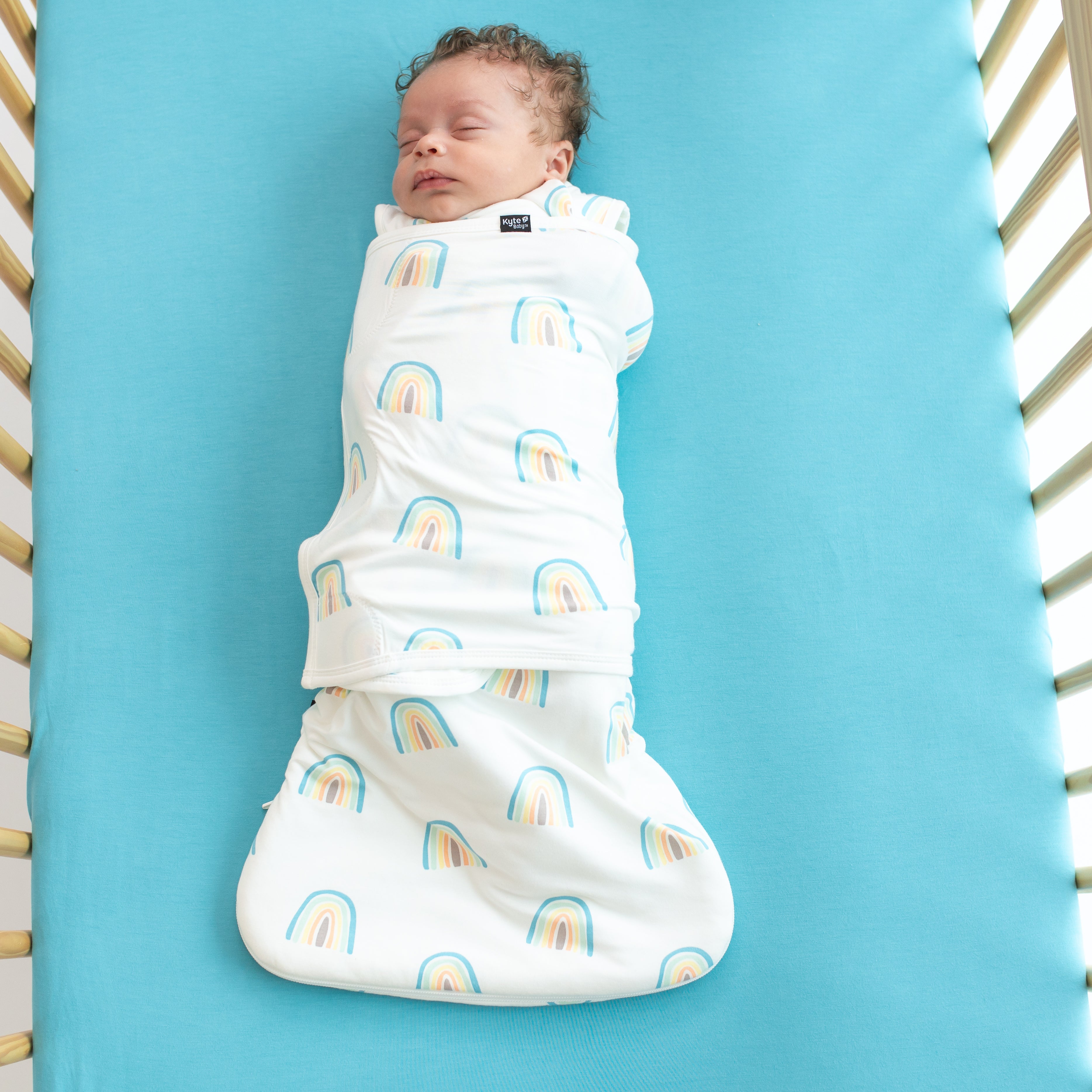 Baby asleep in Sleep Bag Swaddler in Makai Rainbow 1.0 on a makai crib sheet