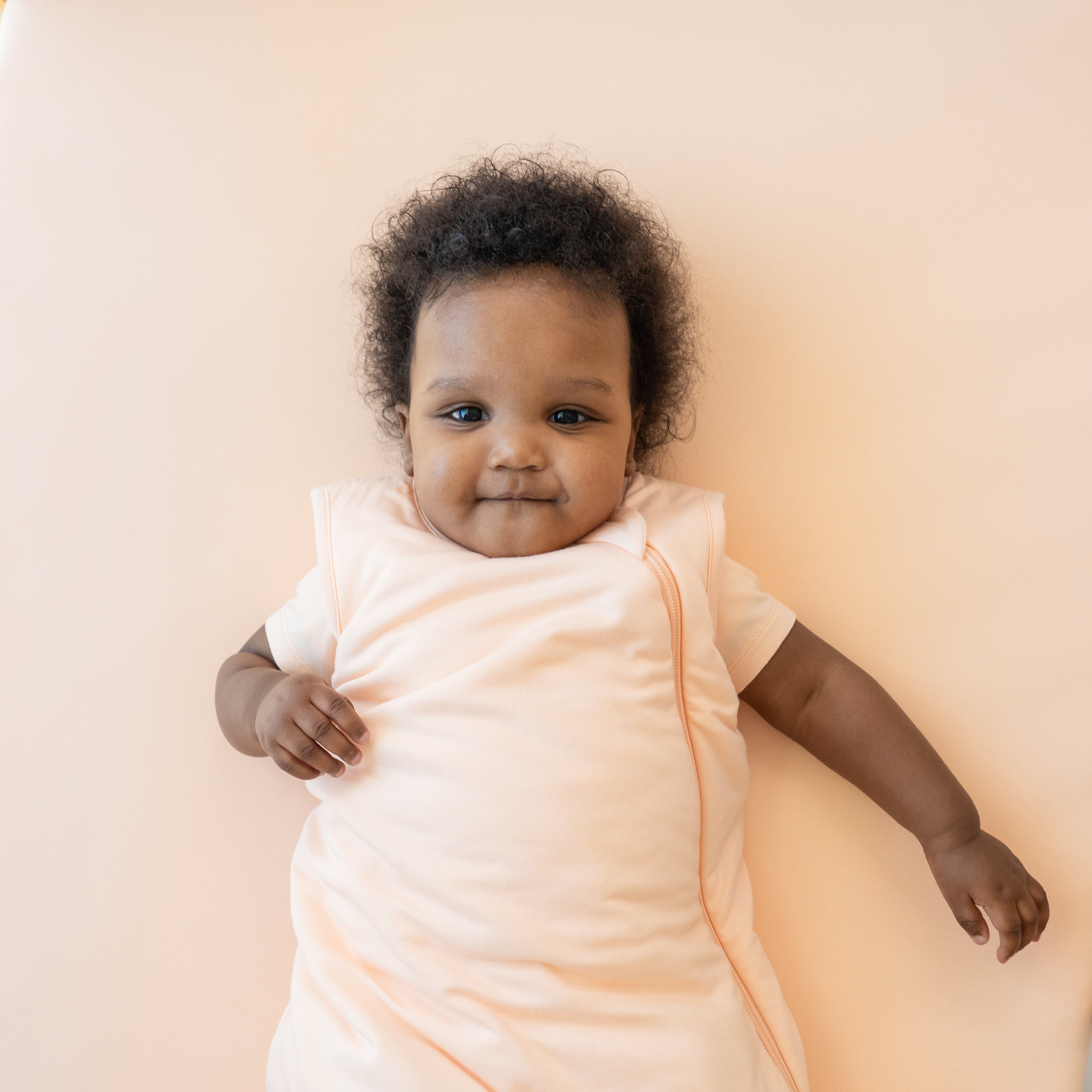 Infant model wearing the Sleep Bag in Canyon 1.0 laying on a Canyon Blanket