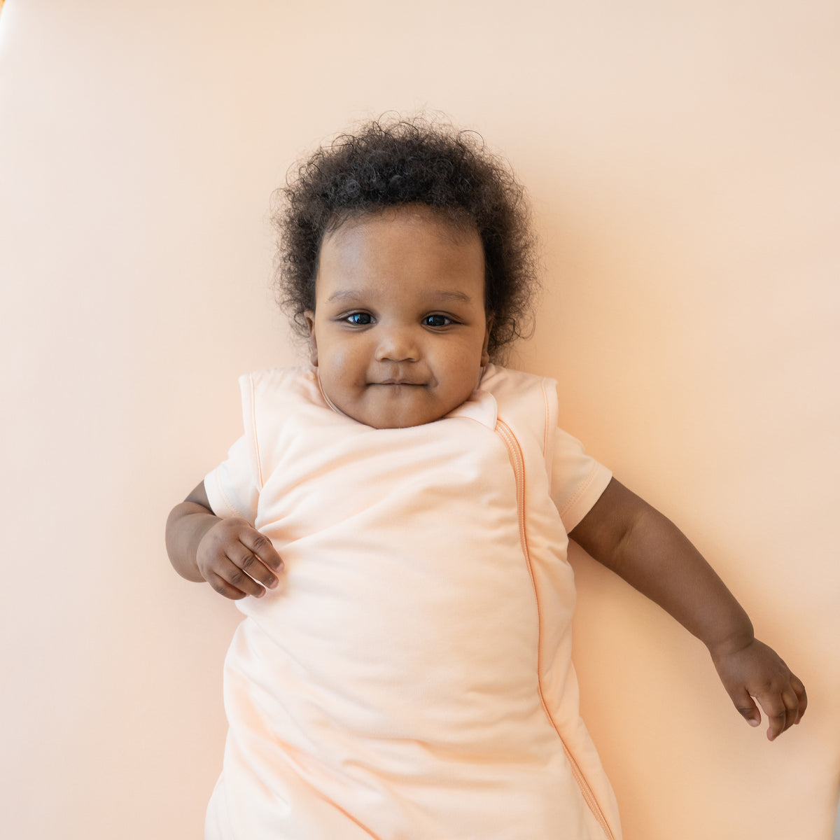 Infant model wearing the Sleep Bag in Canyon 1.0 laying on a Canyon Blanket