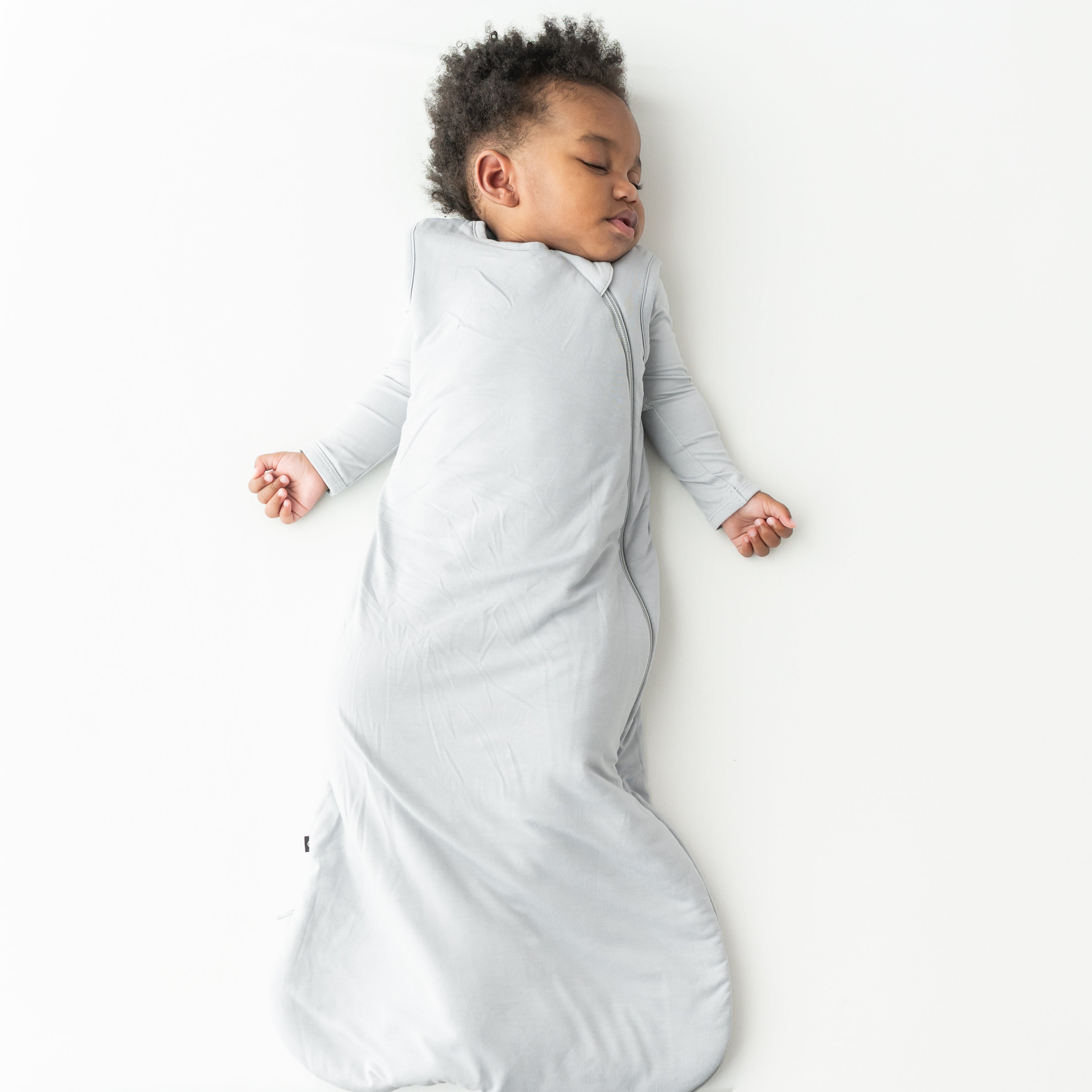 Child sleeping in a buttery soft, gray sleep bag on a white background