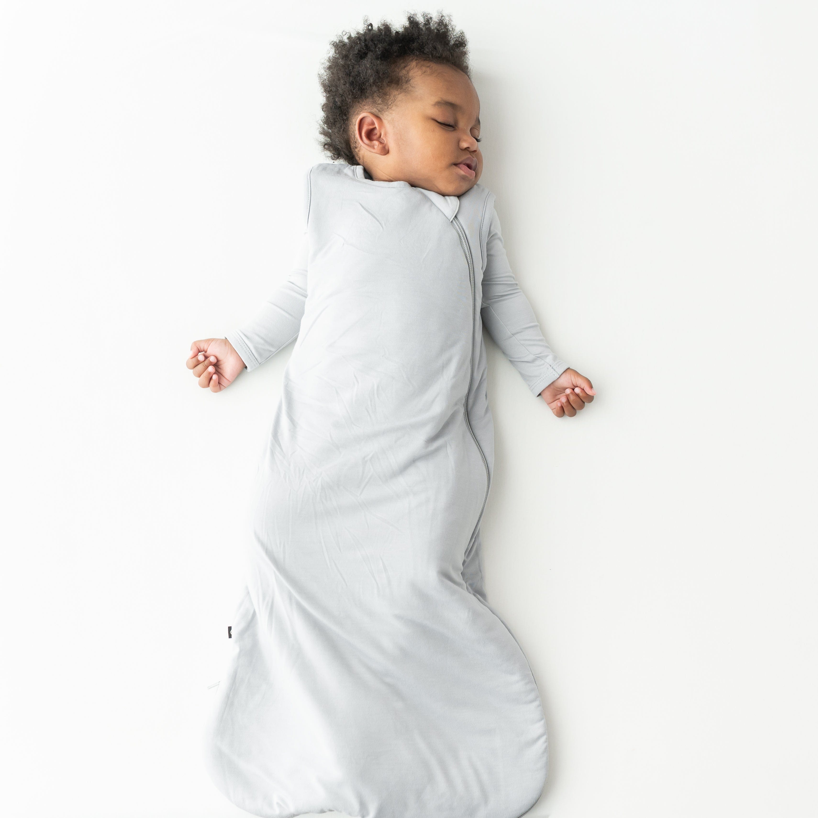 Child sleeping in a buttery soft, gray sleep bag on a white background