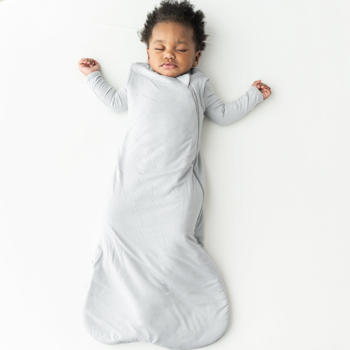 Child sleeping in a gray soft bamboo wearable blanket on a white background