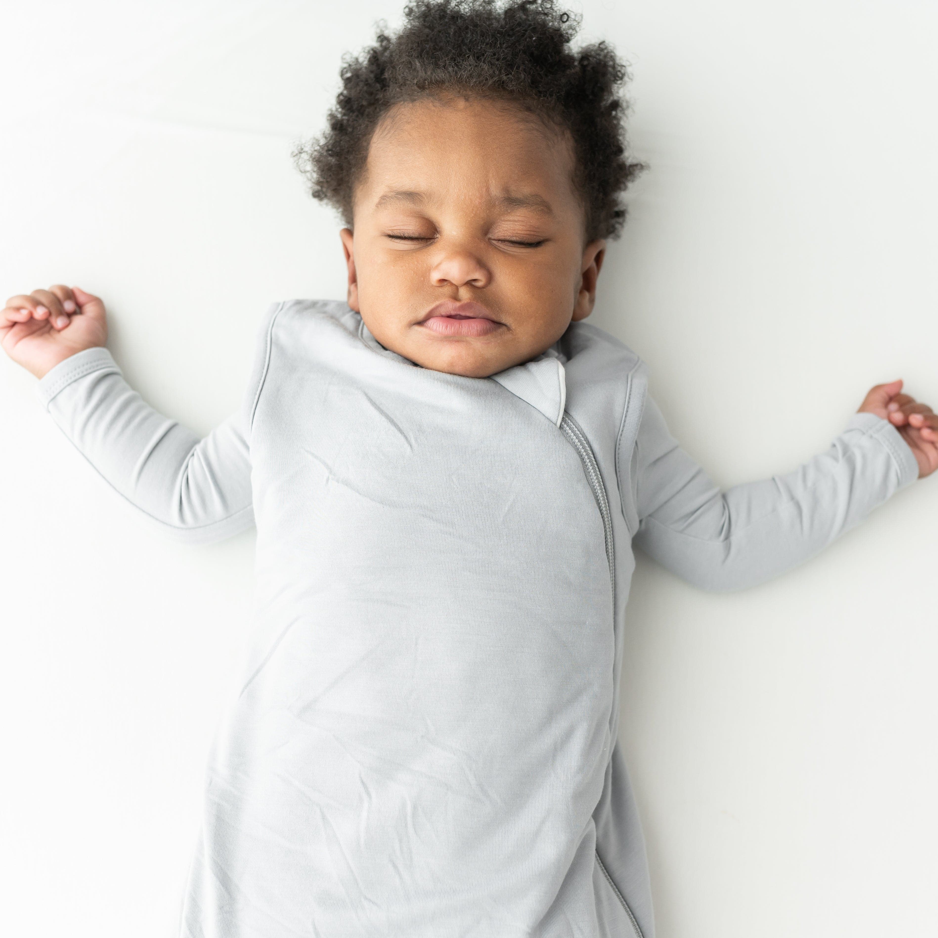 Baby sleeping in a light gray sleep bag on a white background